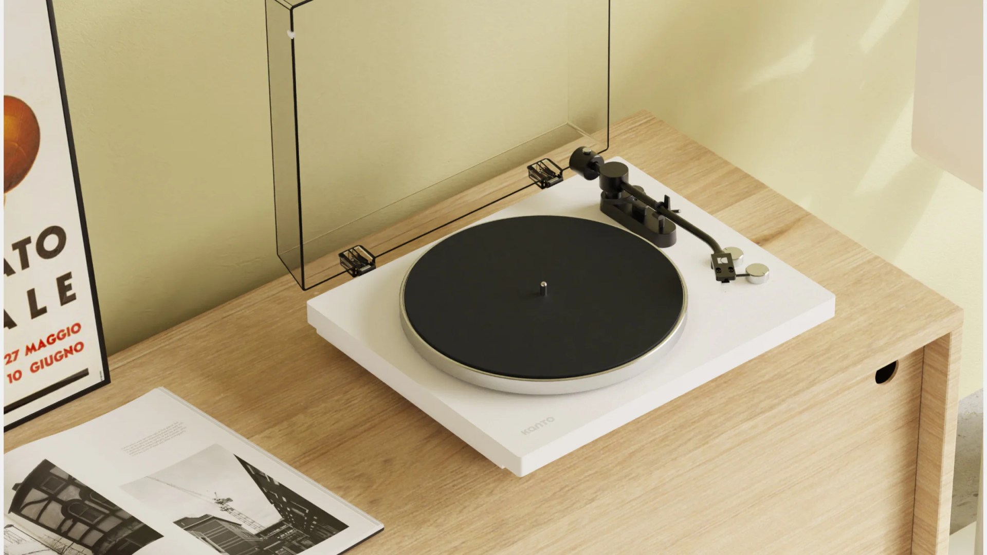 White Kanto turntable with black platter and tonearm on a light wood desk with a clear dust cover open.