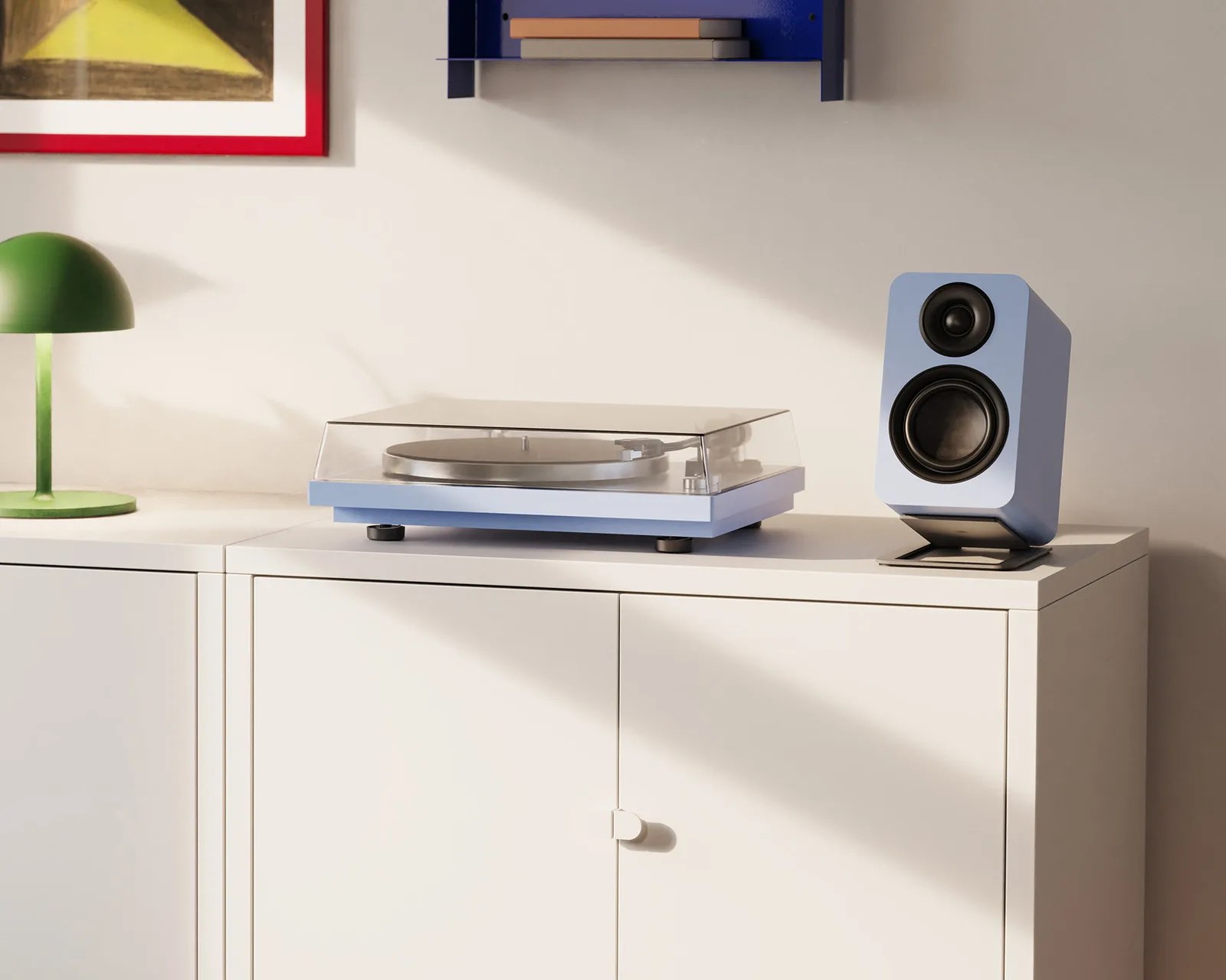Light blue turntable with clear dust cover and matching speaker on white cabinet next to green dome lamp.