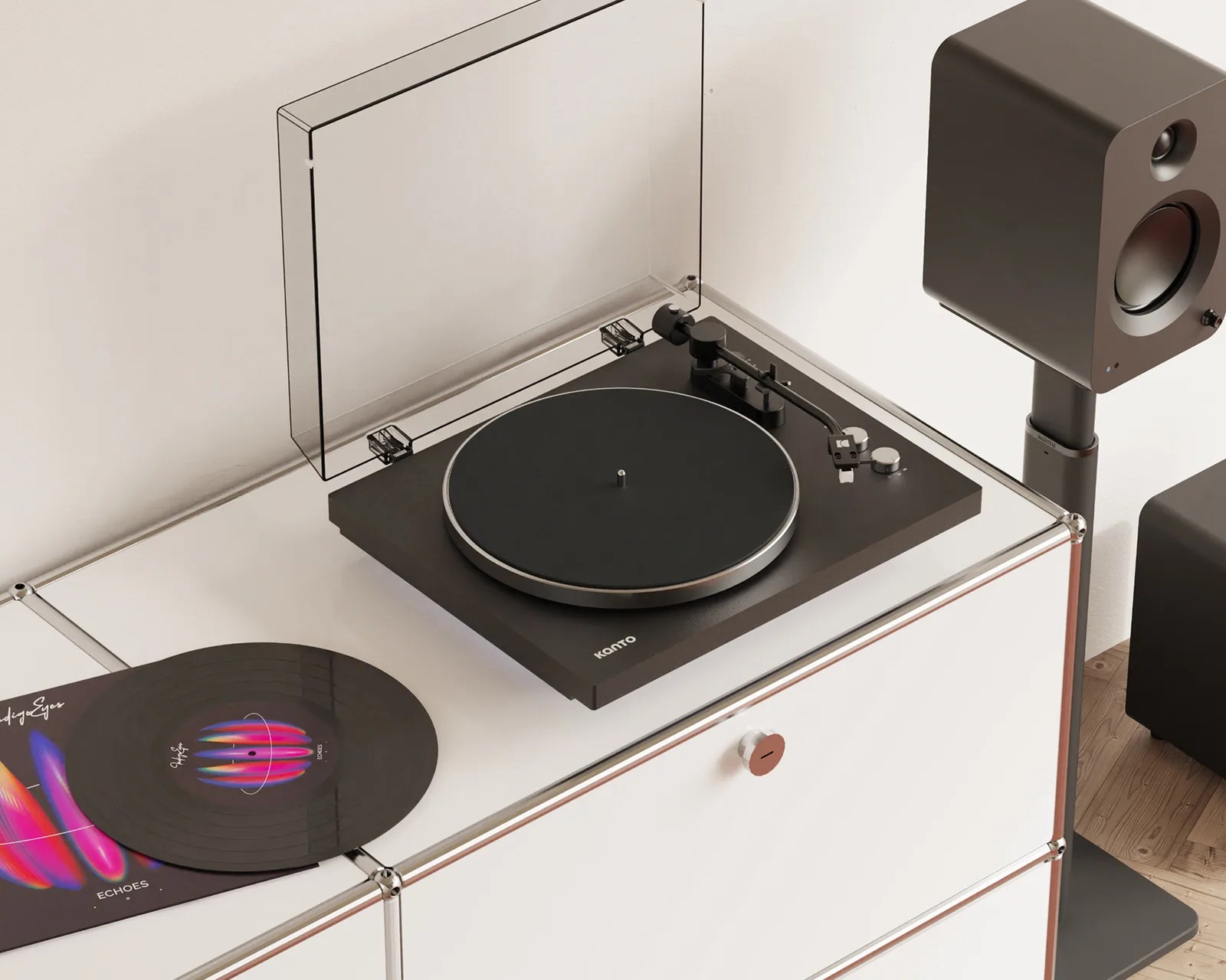 Black Kanto turntable with transparent dust cover on white cabinet next to black speaker on stand.