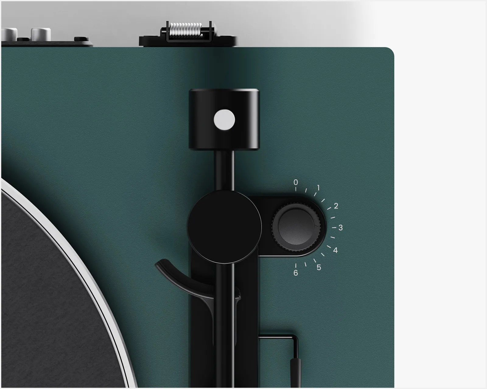 Close-up of a black tonearm and adjustment dial on a dark green turntable.