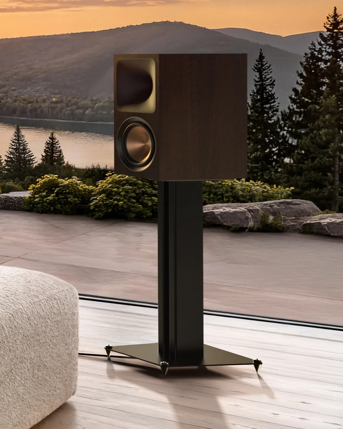 Dark wood bookshelf speaker with copper driver on a black metal stand in a room with a mountain view.