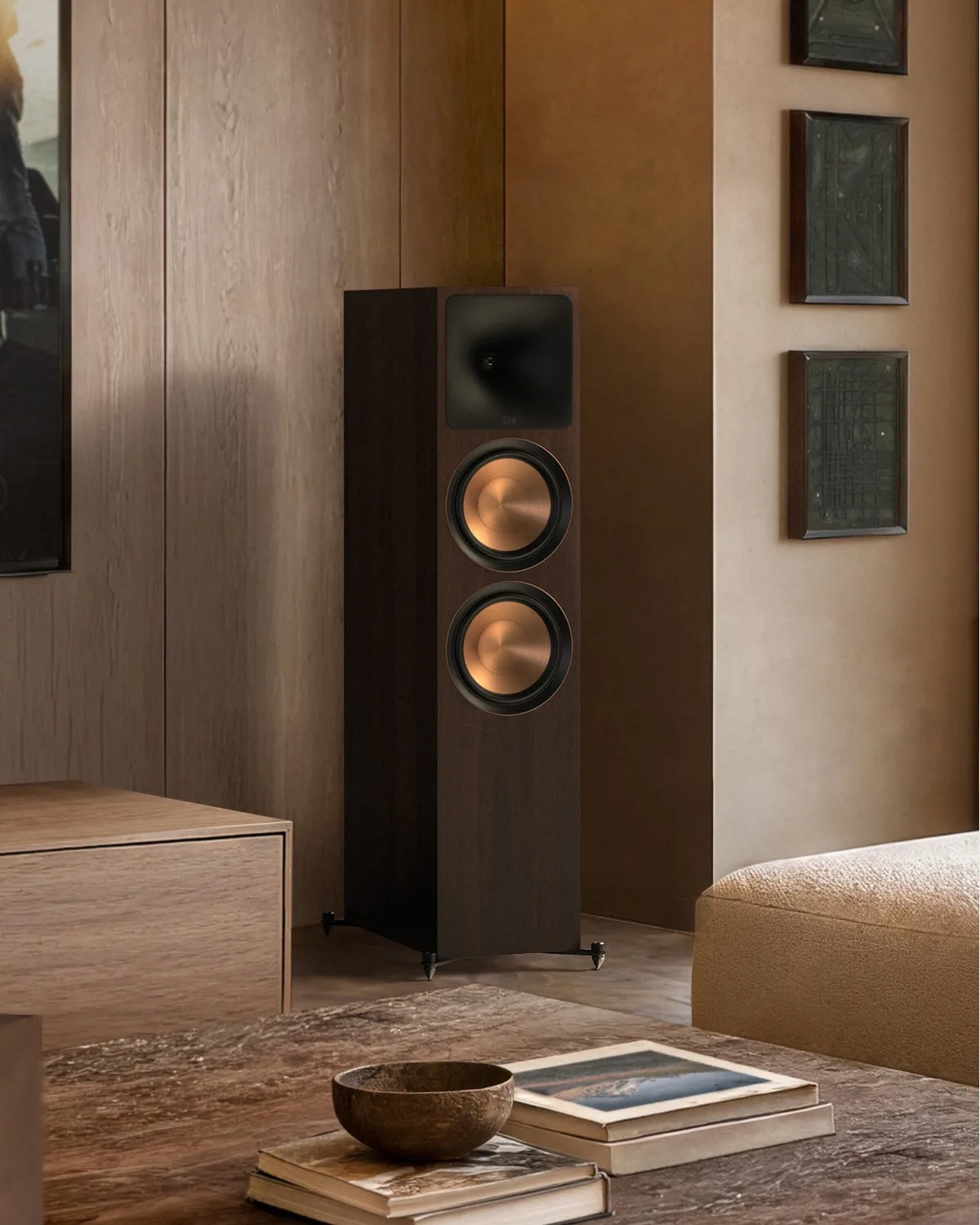 Tall dark wood floor-standing speaker with two copper-colored drivers in a modern living room corner.