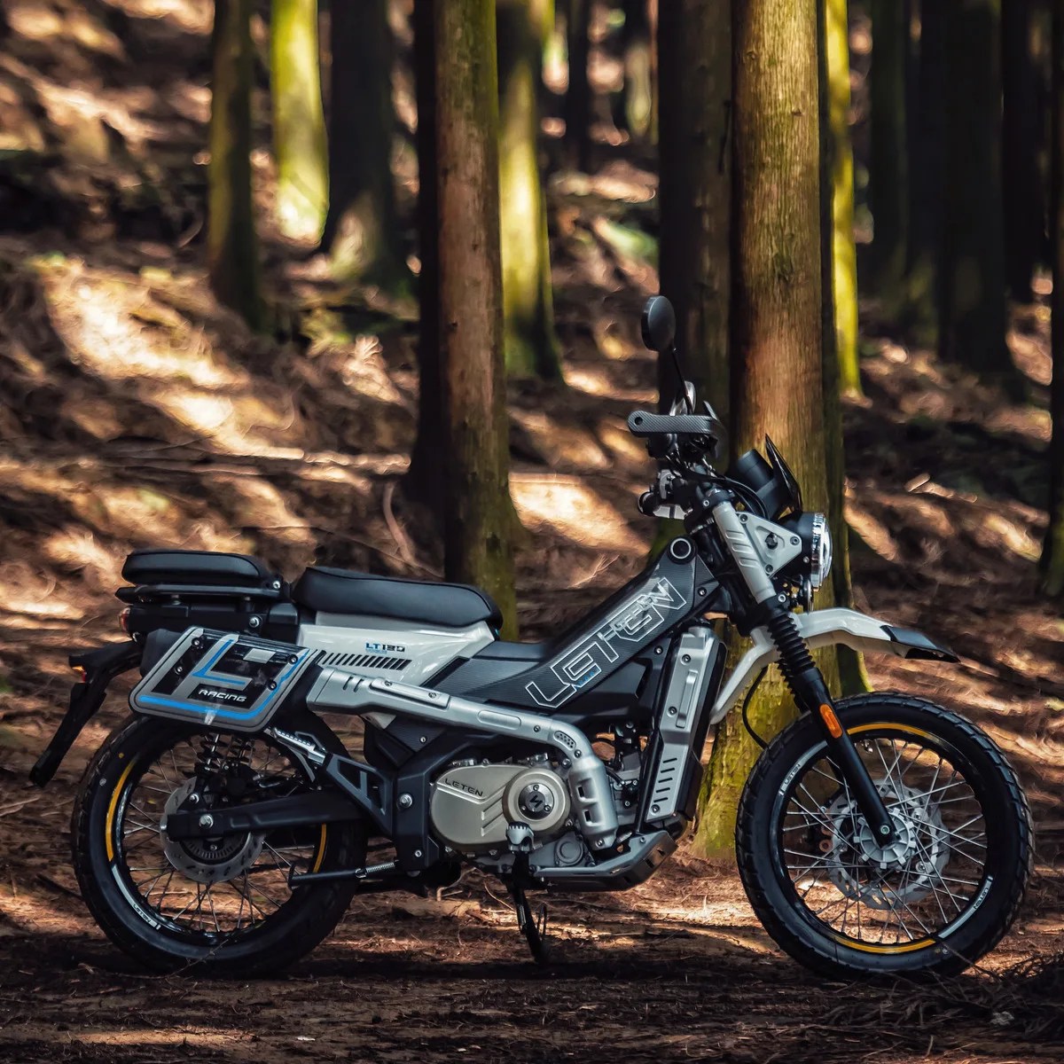 Silver and black Leten LT180 motorcycle with off-road tires parked in a forest.