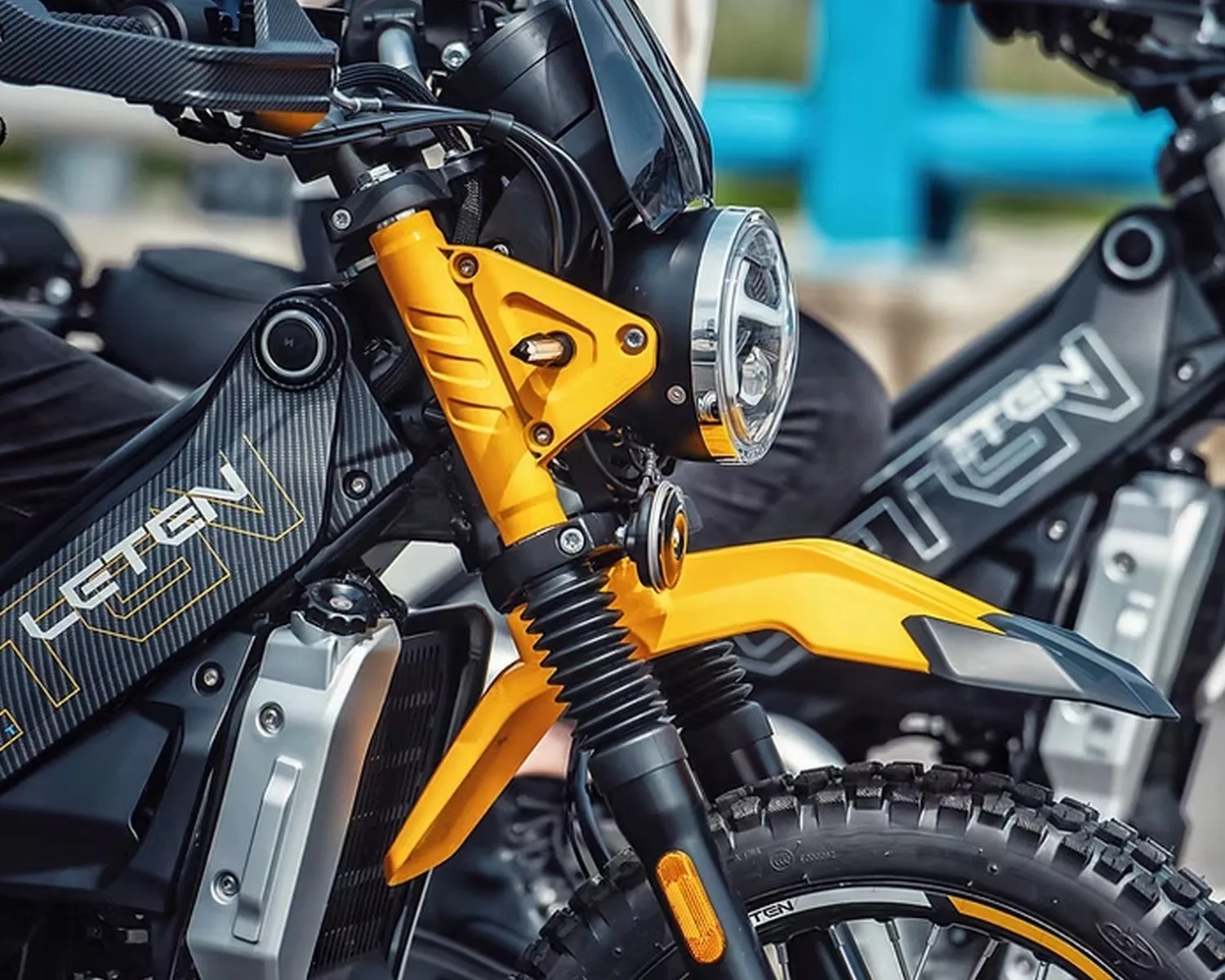 Close-up of a yellow and black electric motorcycle front with a round headlight and knobby tire.