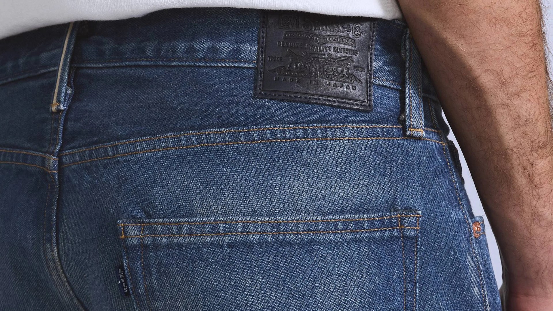 Close-up of blue Levi's denim jeans back pocket with black leather brand patch and a person's arm beside it.