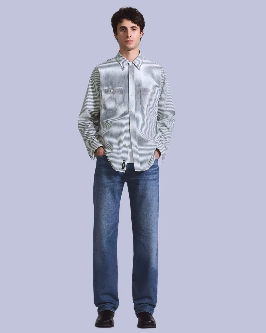 Man wearing a light blue and white vertical striped button-up shirt with blue jeans and black shoes.