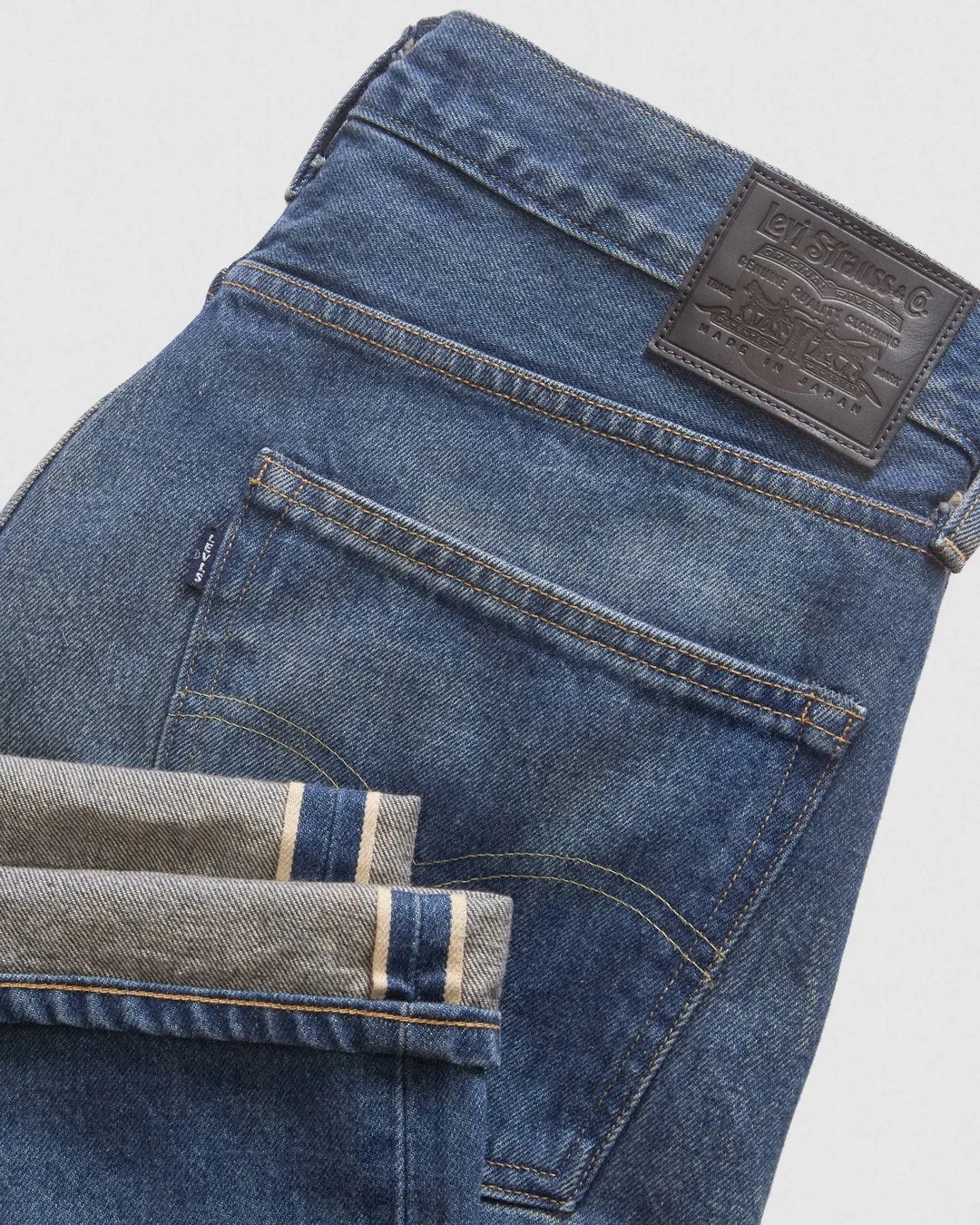 Folded blue denim Levi's jeans showing back pocket, leather brand patch, and selvedge edge.
