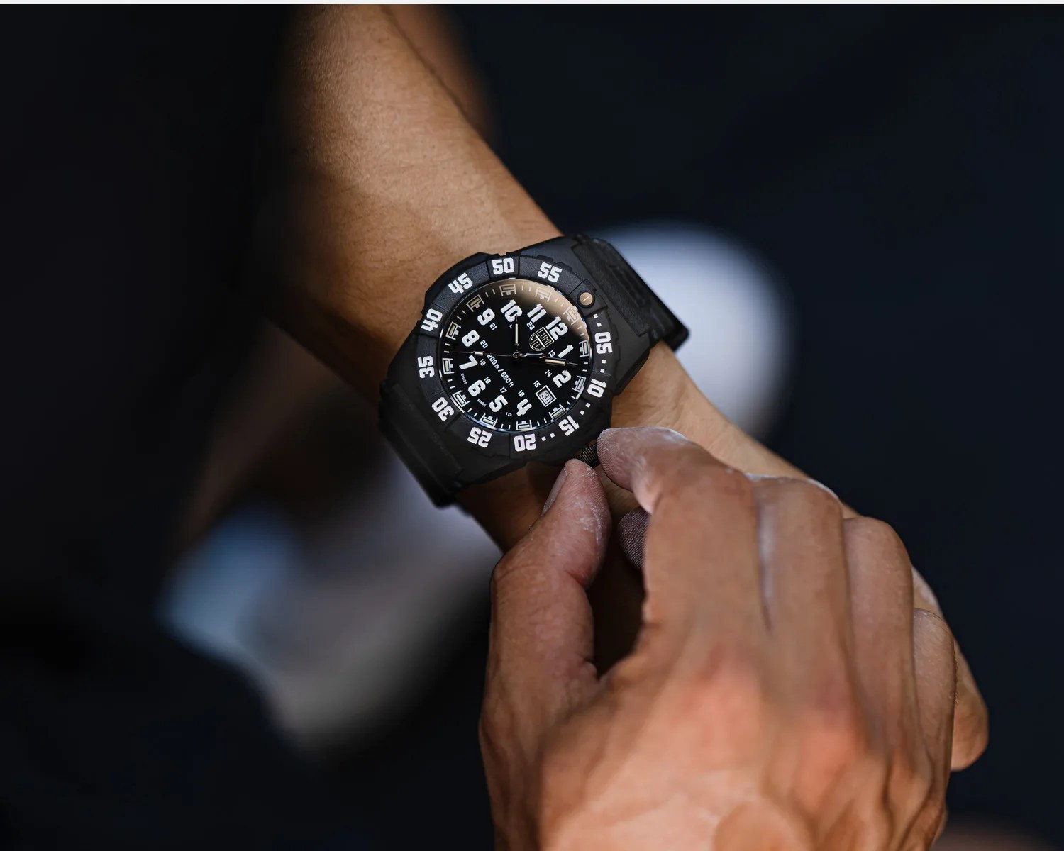 Black tactical wristwatch with white numerals and rotating bezel worn on a wrist, adjusted by a hand.