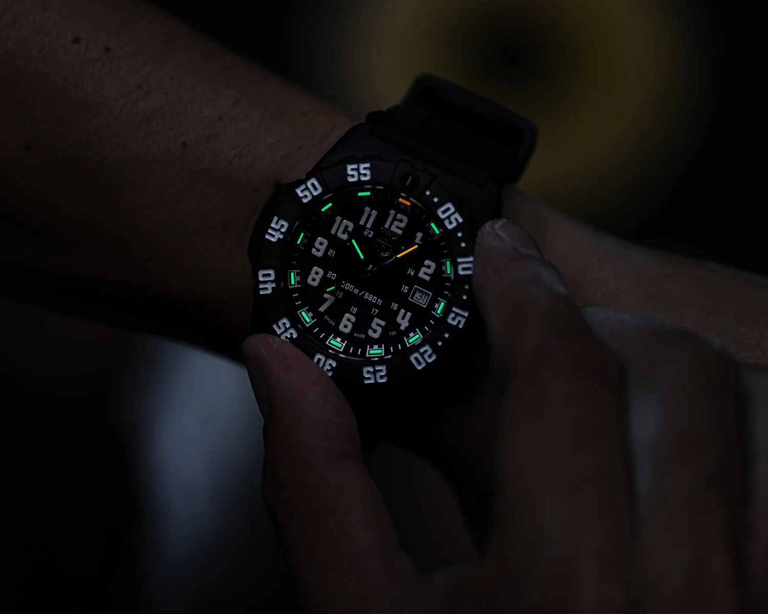 Black wristwatch with luminous green and orange hands and white numerals on a dark wrist.