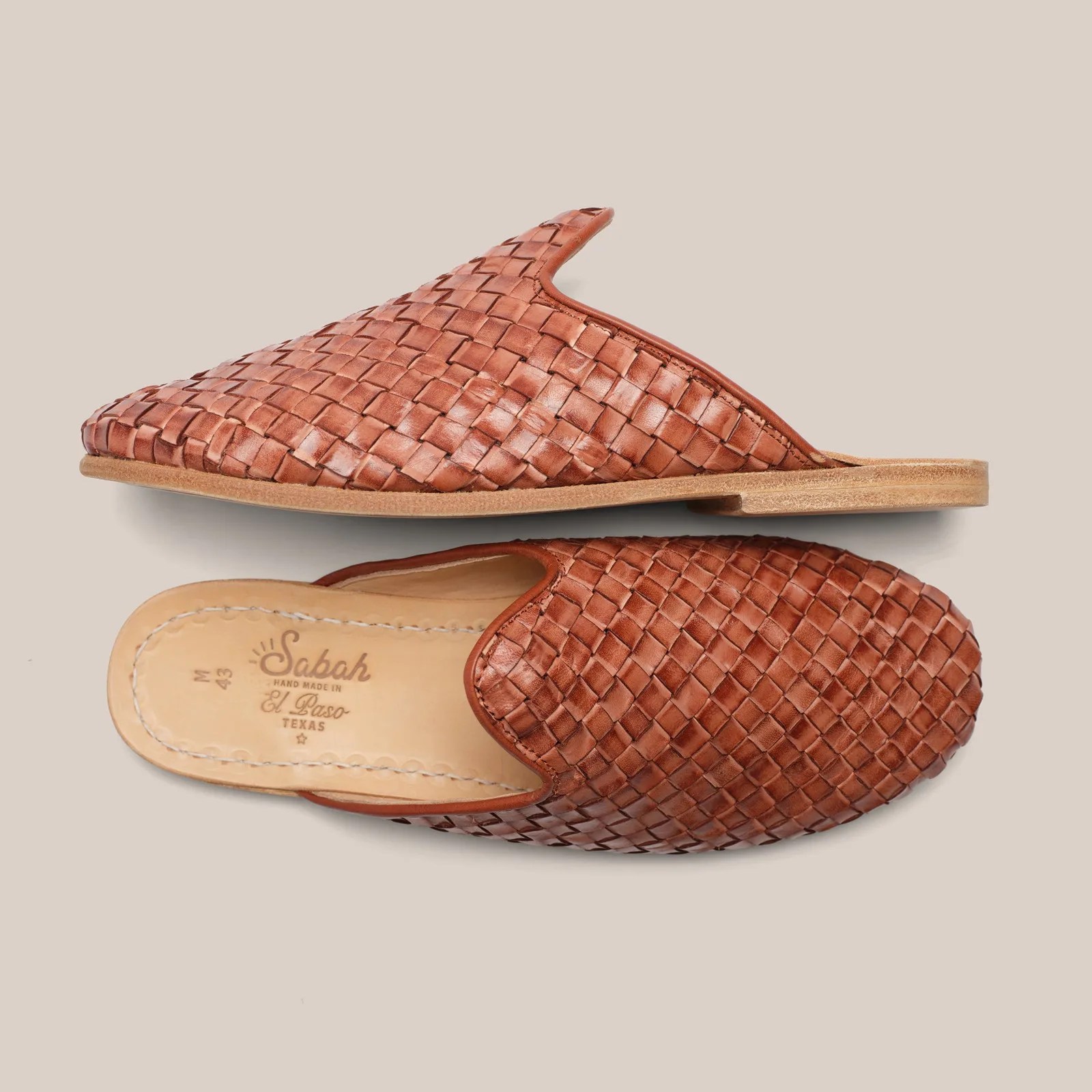 Pair of brown woven leather slip-on shoes with flat wooden soles on a beige background.