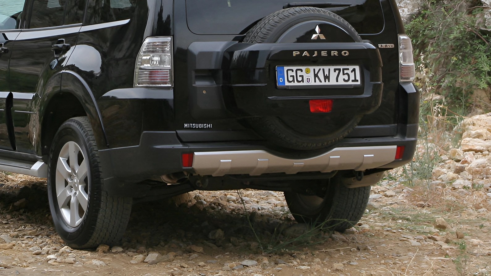 Rear view of a black Mitsubishi Pajero SUV with spare tire mounted on the back, parked on rocky terrain.