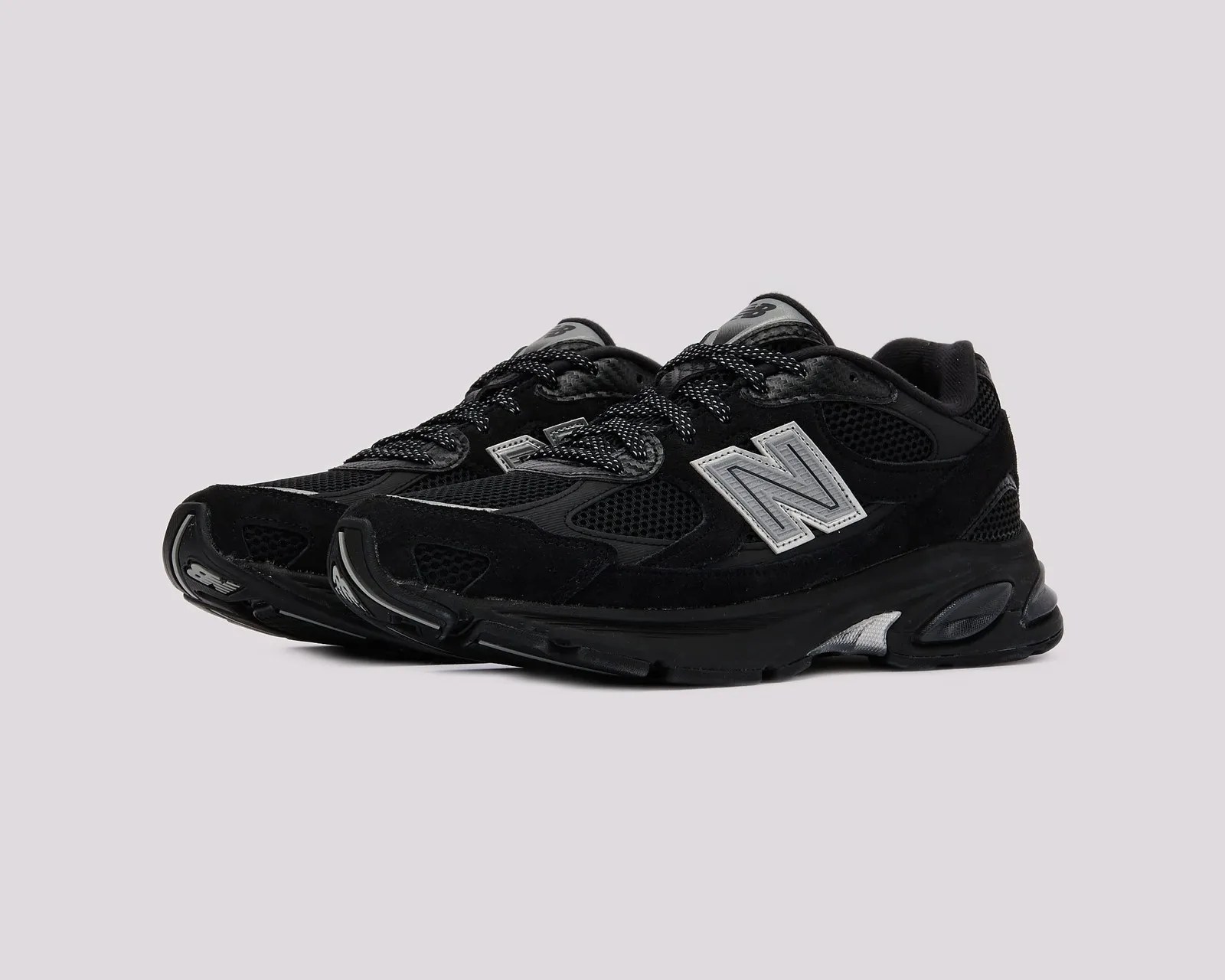 Pair of black New Balance sneakers with mesh and suede panels and reflective silver "N" logos on the sides.