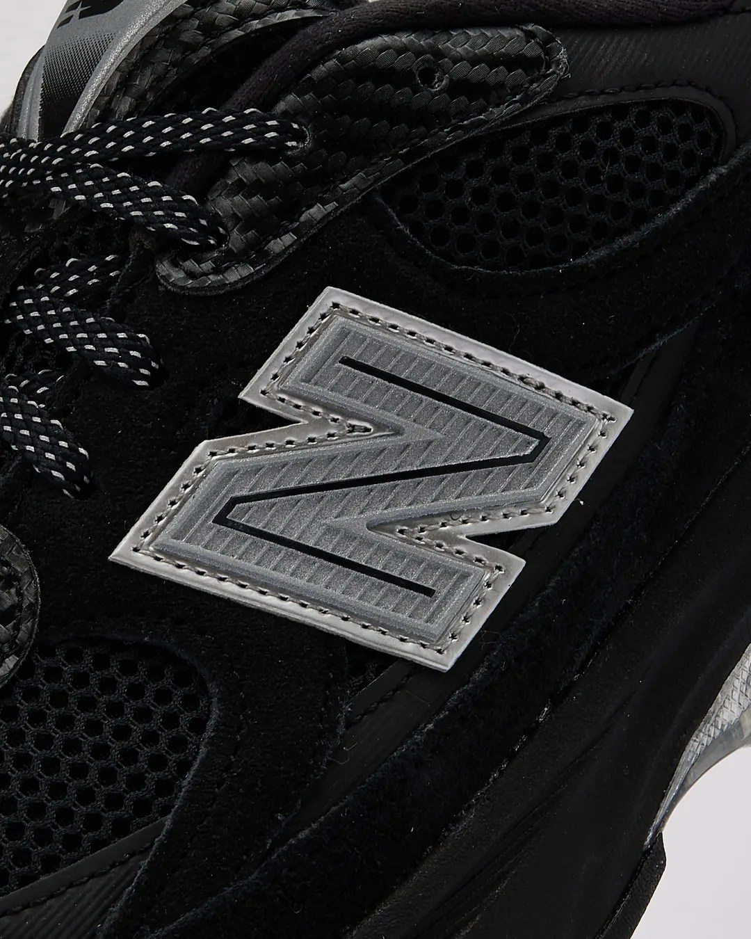 Close-up of black New Balance sneaker with reflective silver "N" logo and black-and-white patterned laces.