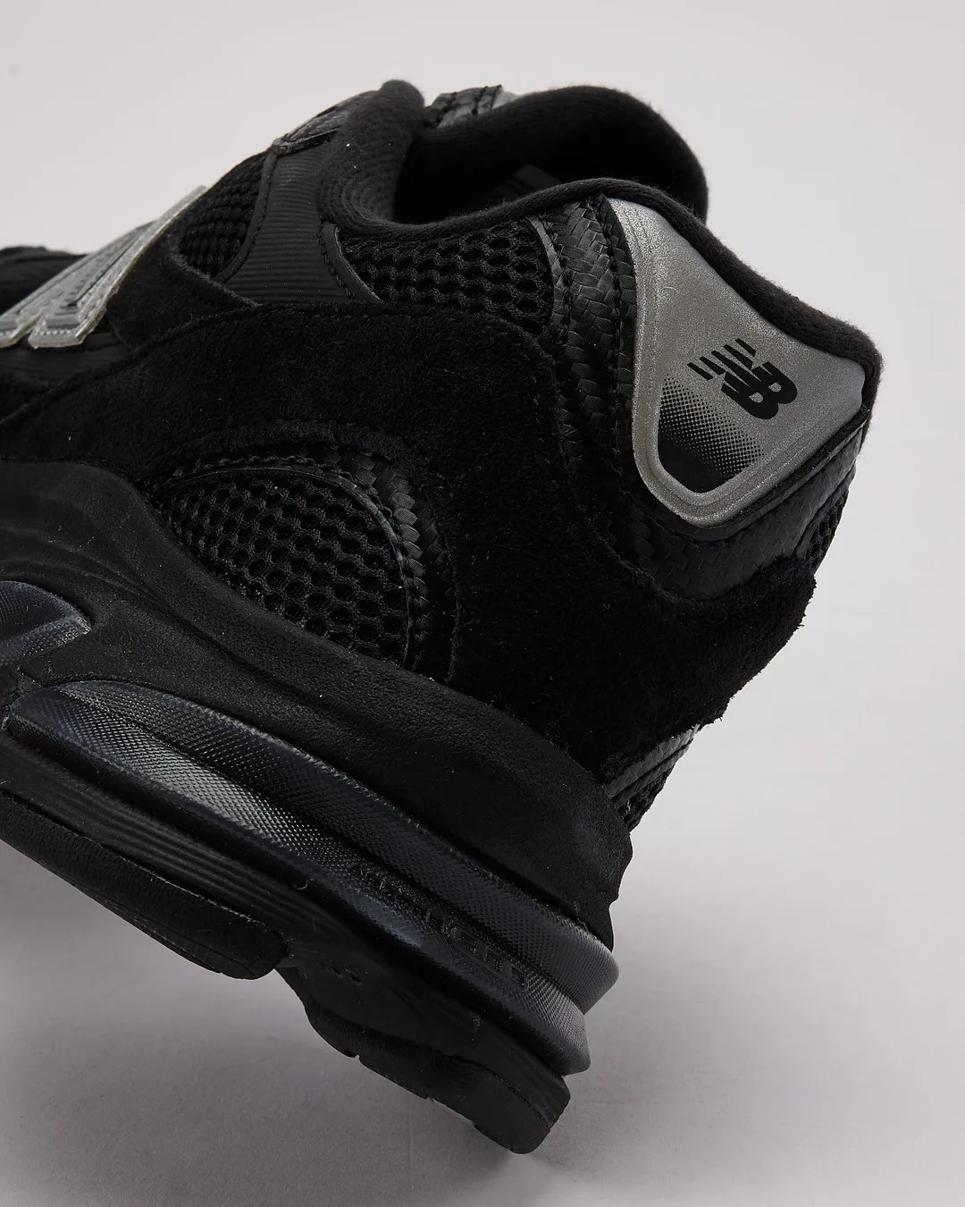 Close-up of the black New Balance sneaker heel with mesh, suede, and reflective silver logo detail.