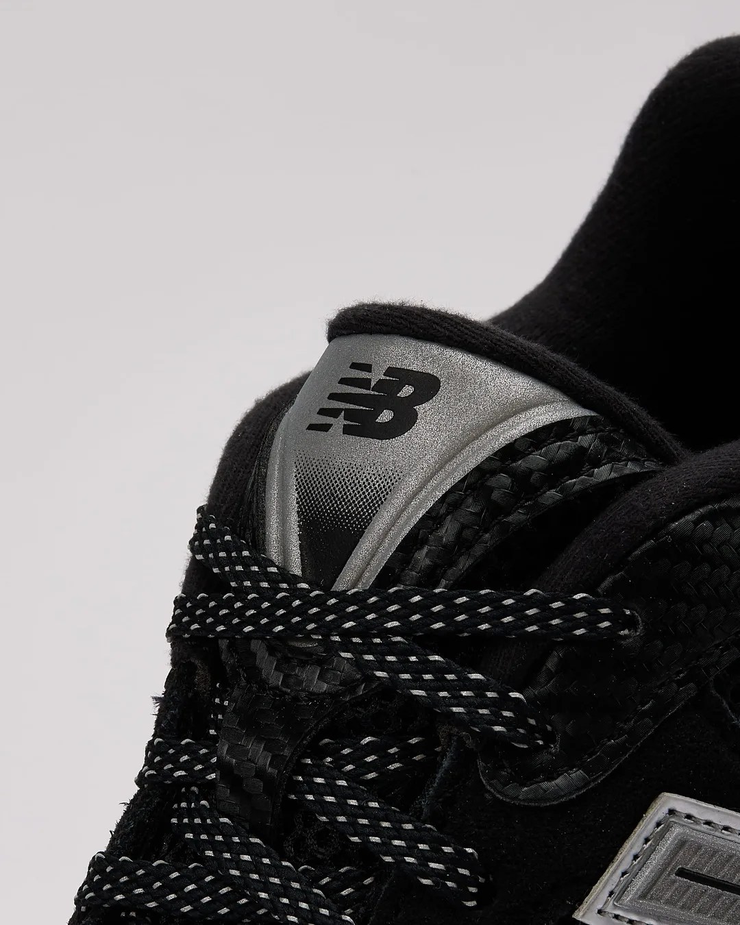 Close-up of black New Balance sneaker tongue with silver logo and black-and-white patterned laces.