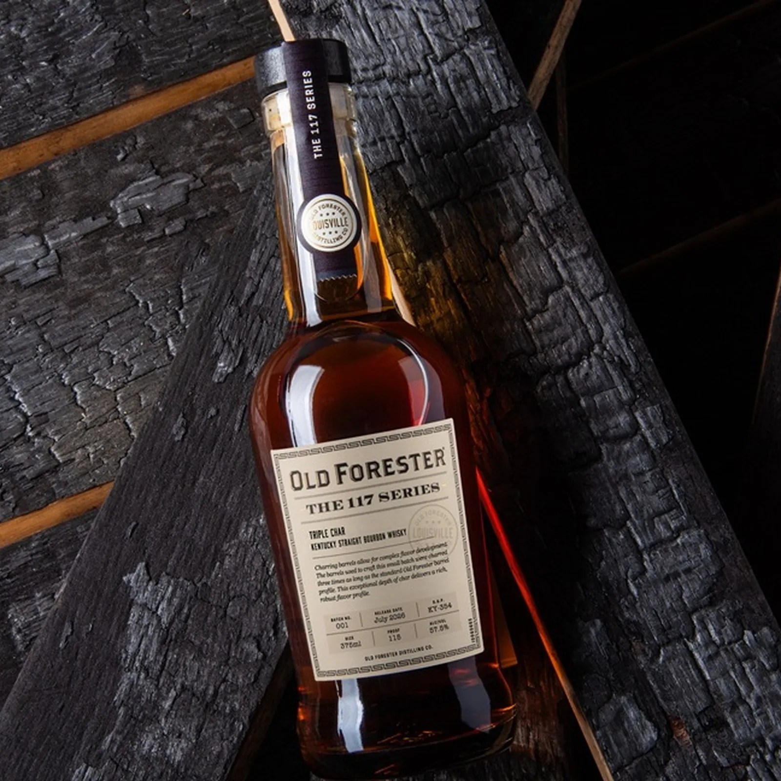 Bottle of Old Forester The 117 Series Triple Oak Kentucky Straight Bourbon Whiskey on a charred wooden surface.