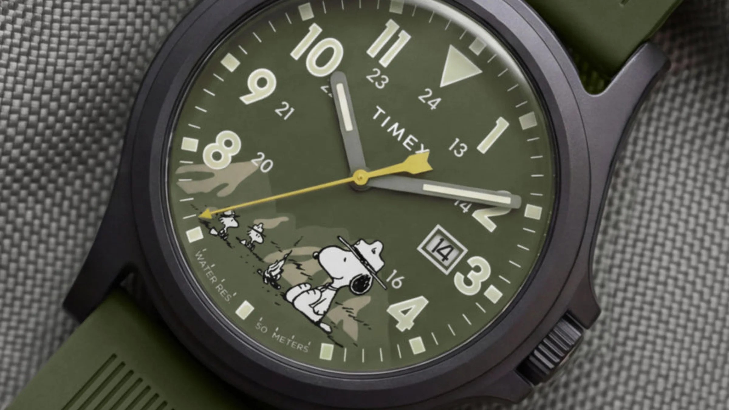 Close-up of a green Timex watch face with Snoopy and Woodstock characters, yellow second hand, and date display.