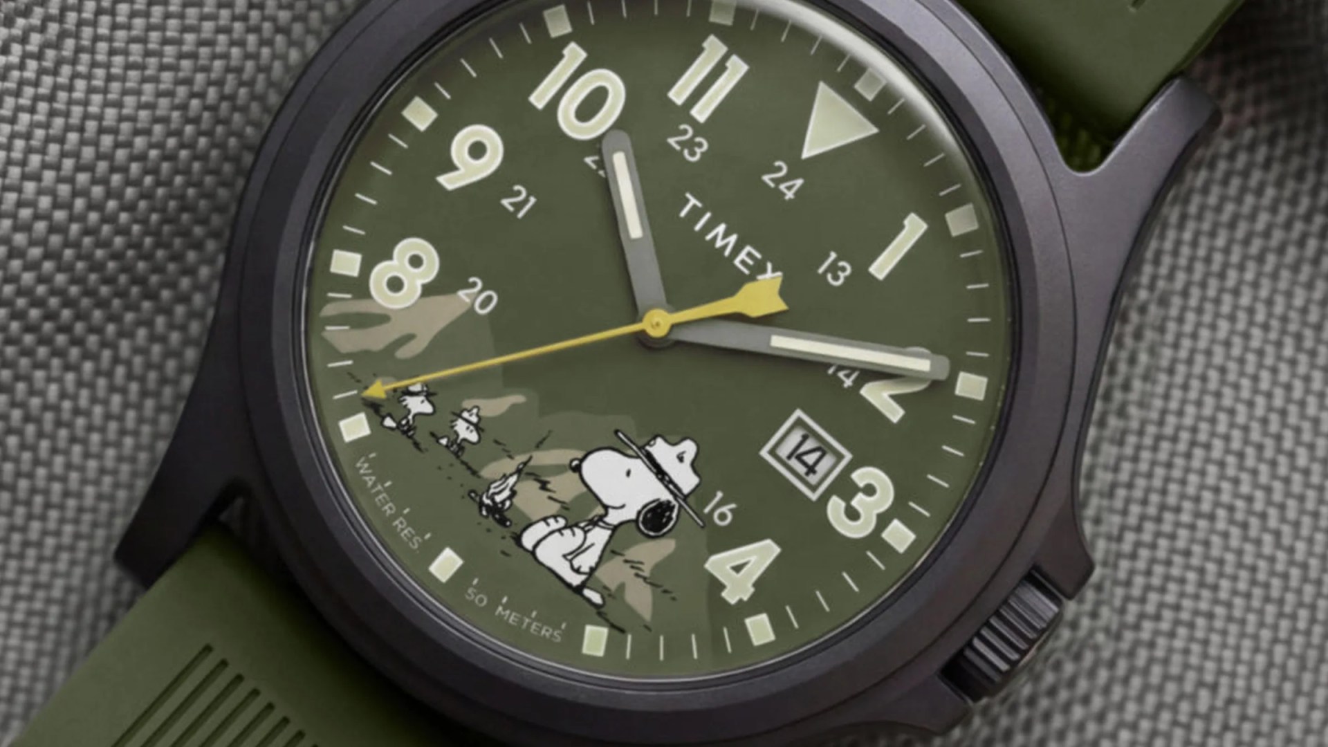 Close-up of a green Timex watch face with Snoopy and Woodstock characters, yellow second hand, and date display.