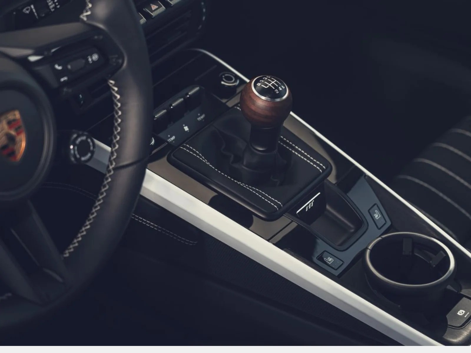 Black leather manual gear shift knob with wooden top and white stitching in a car interior.