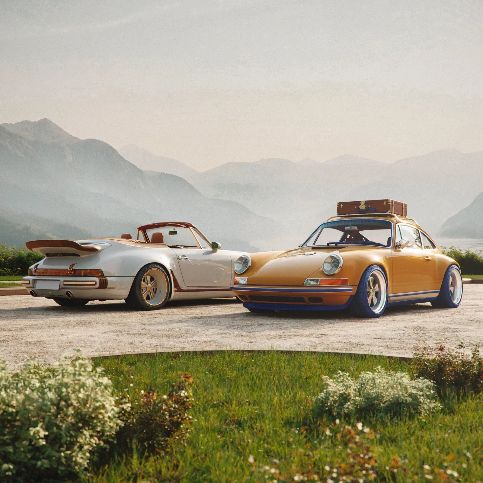 Two vintage Porsche cars, one white convertible and one mustard yellow coupe with a brown suitcase on the roof, parked on a gravel area with mountains in the background.
