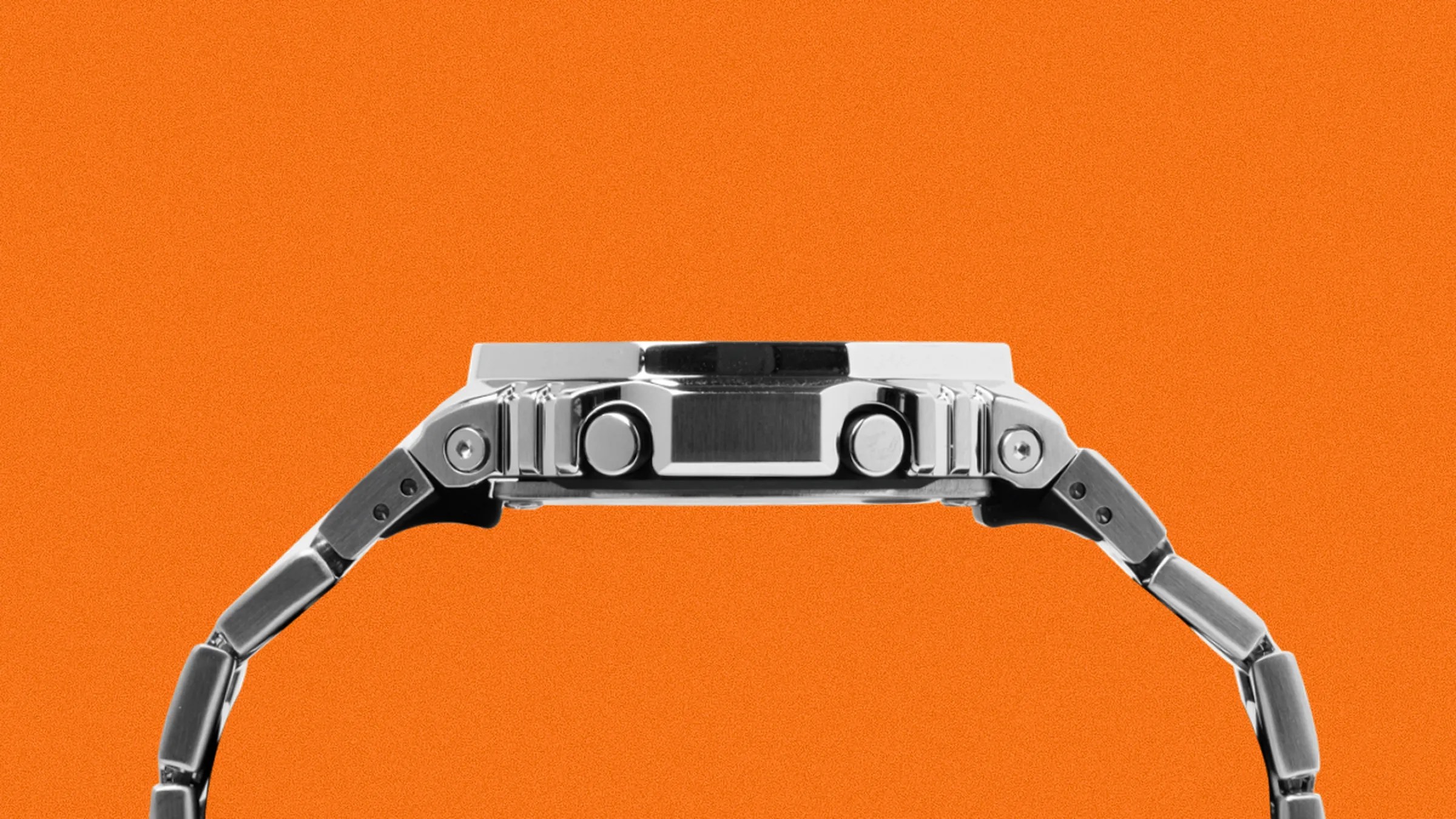 Side view of a silver metal wristwatch with two buttons on the case against an orange background.