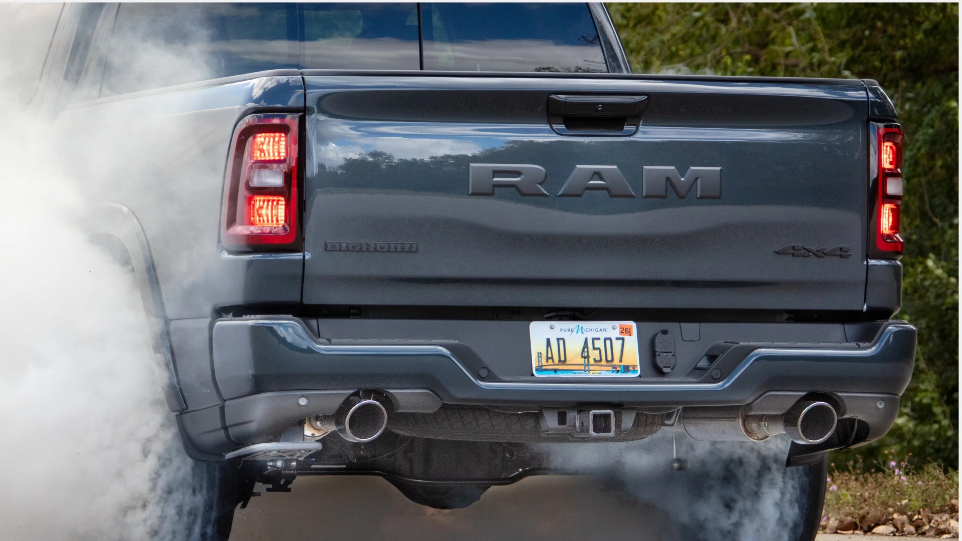 Rear view of a dark gray RAM Bighorn 4x4 pickup truck with Michigan license plate AD 4507, emitting smoke.