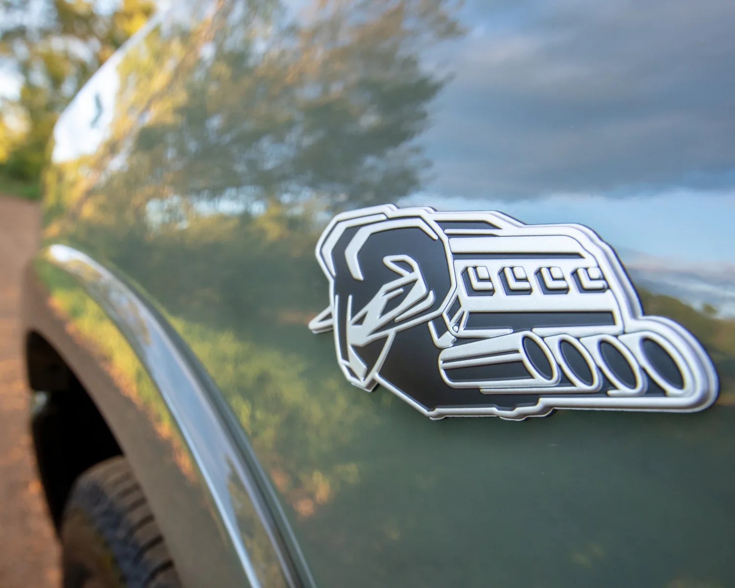 Black and silver engine emblem on a dark green vehicle fender with a blurred background.