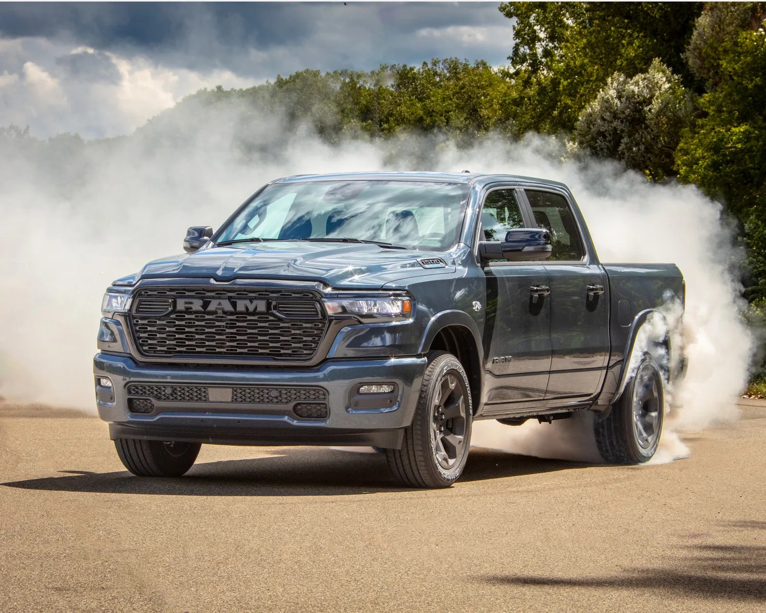 Dark gray RAM 1500 pickup truck performing a burnout on a paved road with smoke around the rear tires.