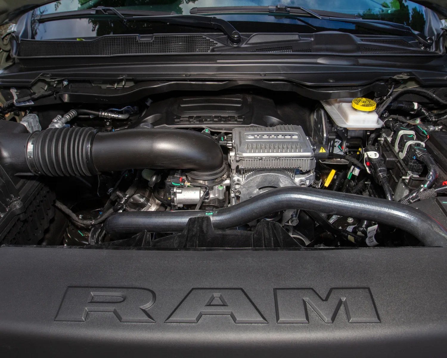 Engine compartment of a RAM vehicle showing black plastic and metal components with RAM logo on the engine cover.