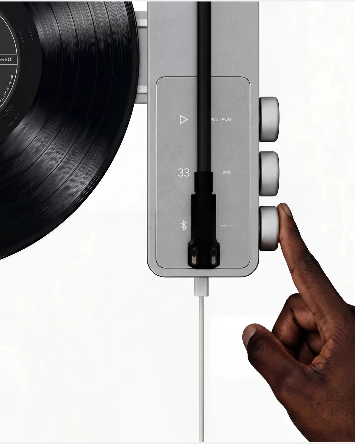 Hand adjusting silver knob on a modern silver and black turntable with a vinyl record.