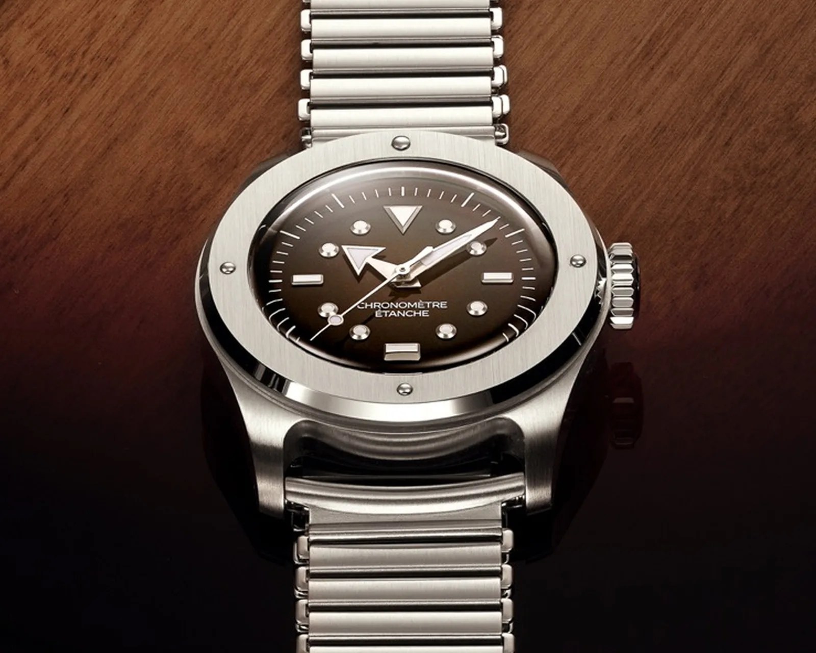 Silver metal wristwatch with a dark dial and bold triangular hour markers on a wooden surface.