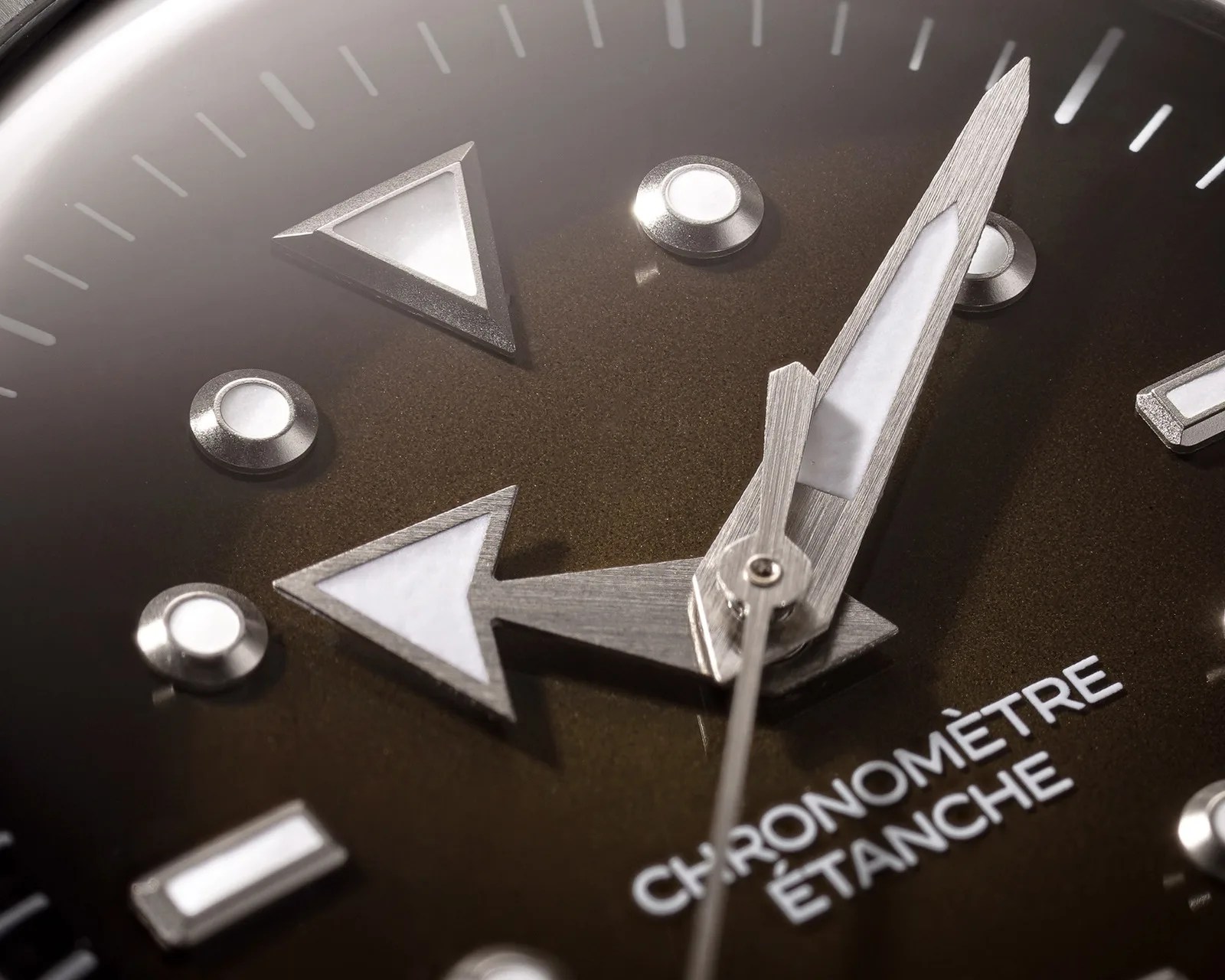 Close-up of a watch face showing silver arrow-shaped hour and minute hands with luminous insets on a dark dial.