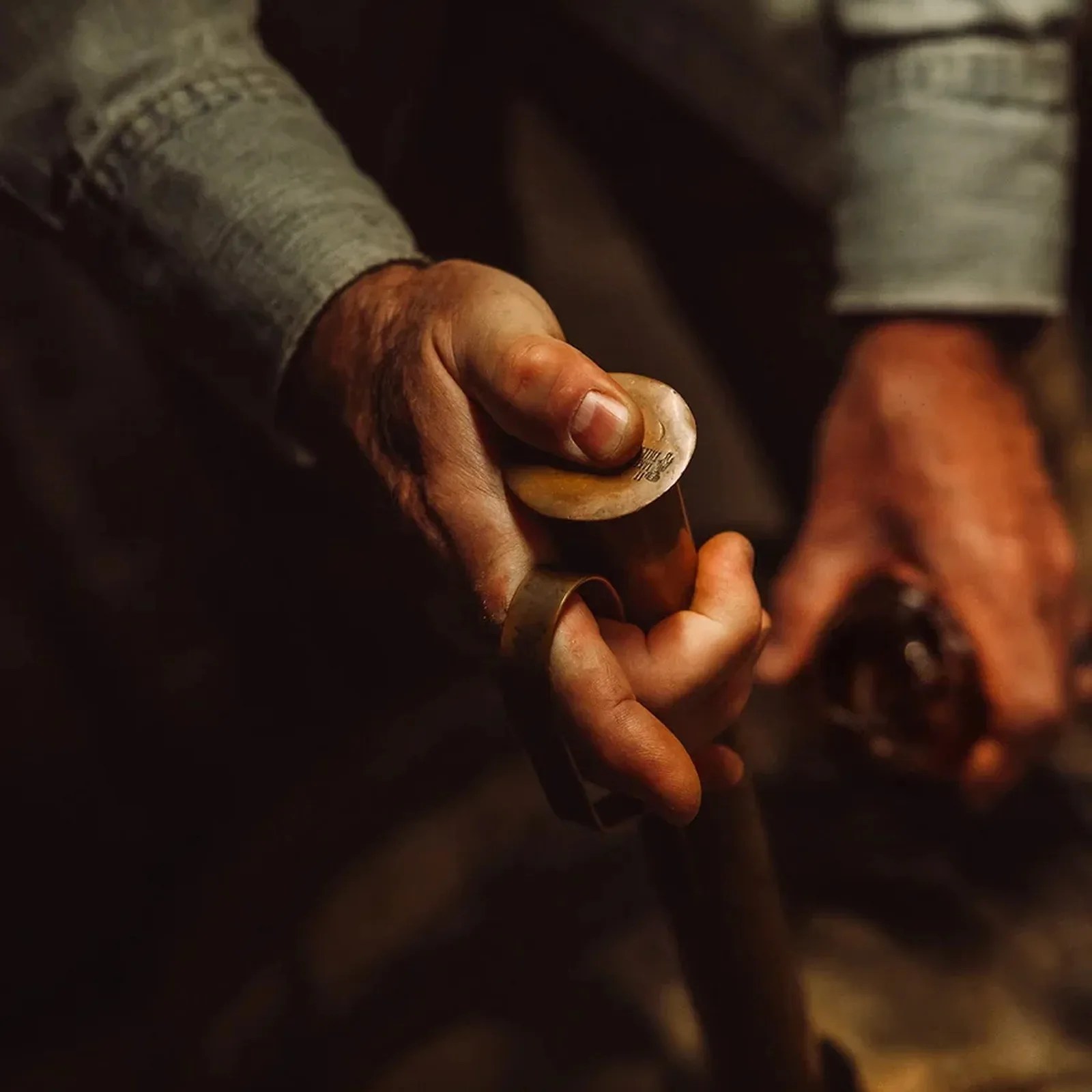 Close-up of a hand holding a brass cymbal finger ring with a strap, worn by a person in a gray sweater.