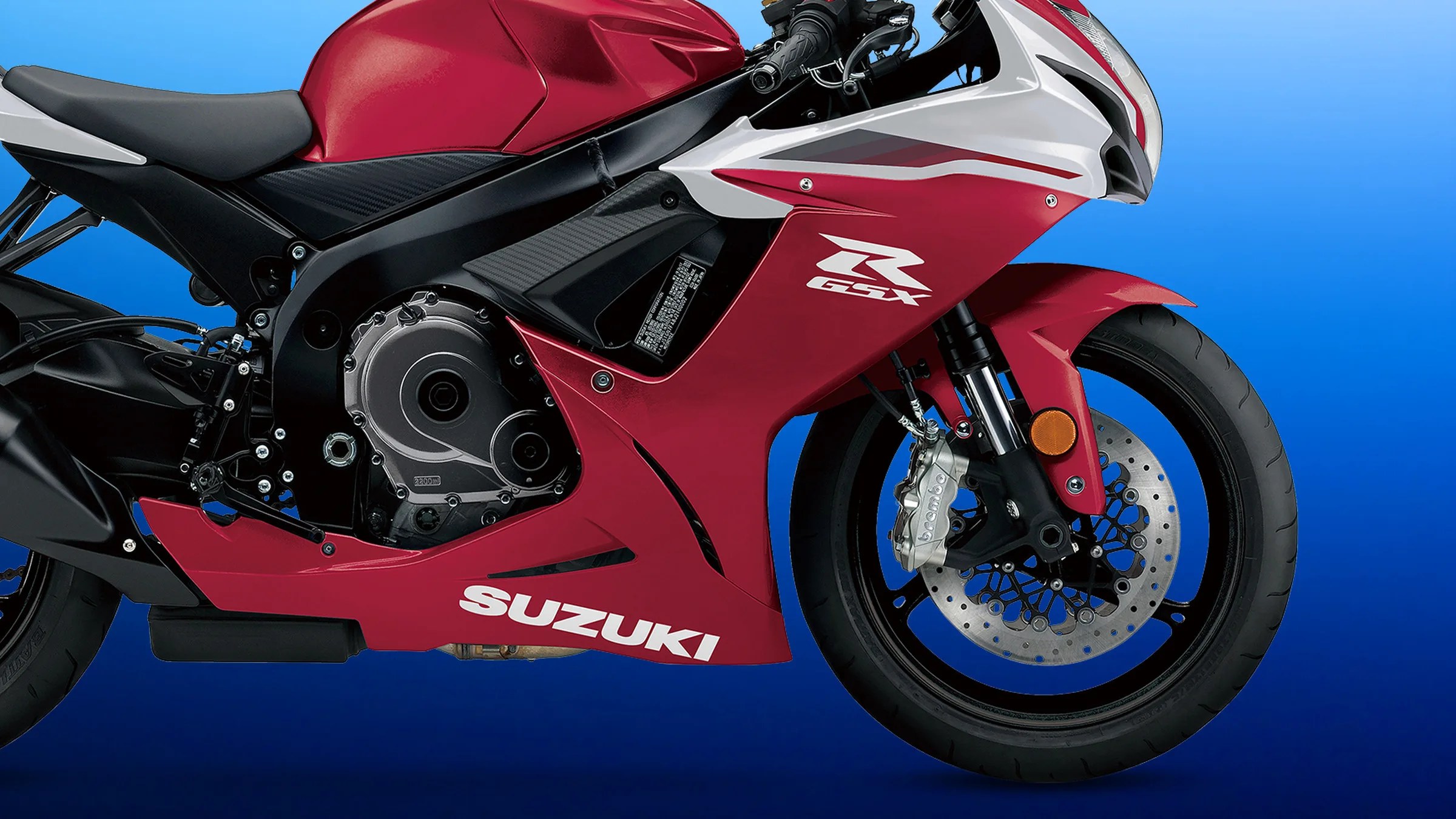Red and white Suzuki GSX sport motorcycle side view showing front wheel, brake disc, and engine details.