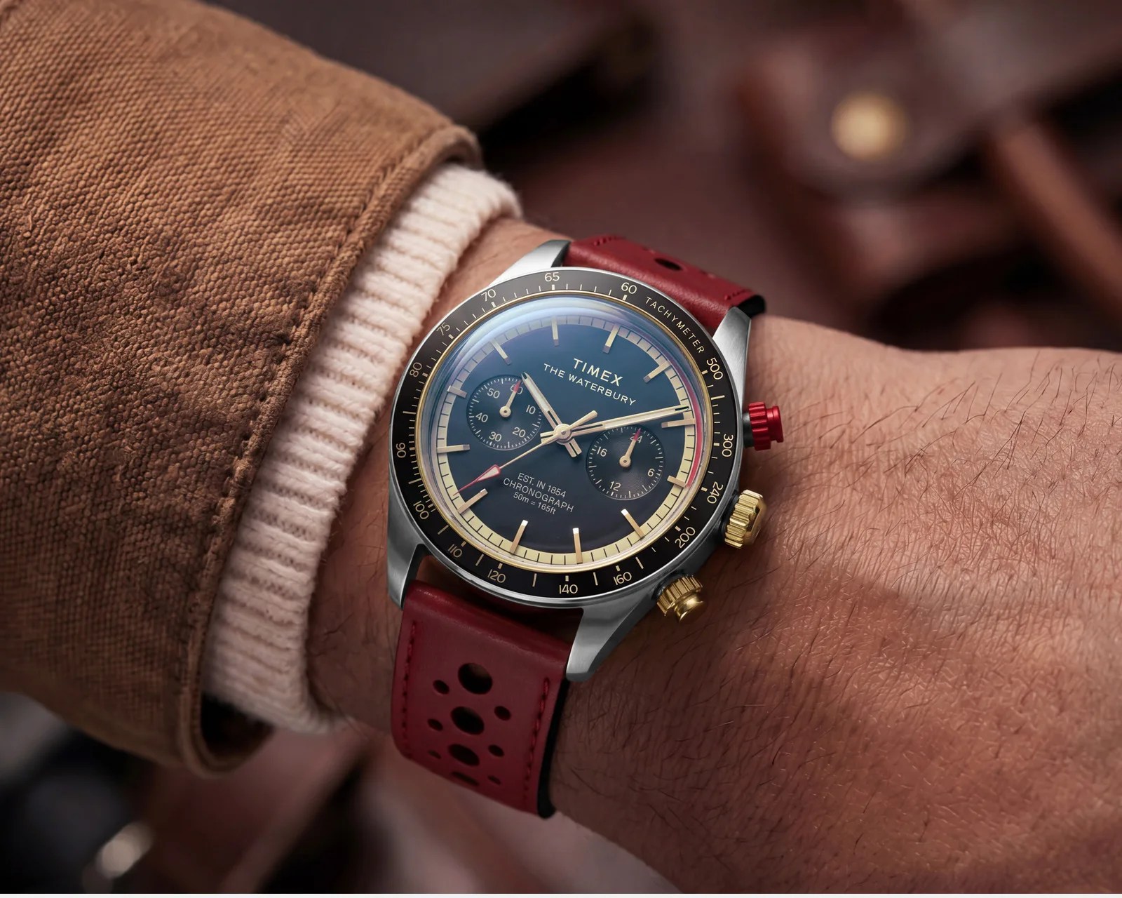 Timex Waterbury chronograph watch with black dial, gold and red accents, and red perforated leather strap on wrist.