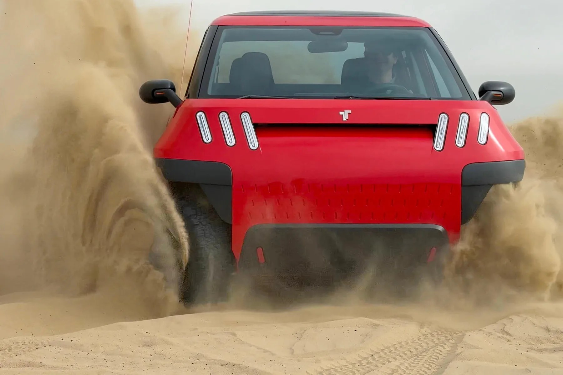 Red electric SUV kicking up sand while driving off-road, front view.