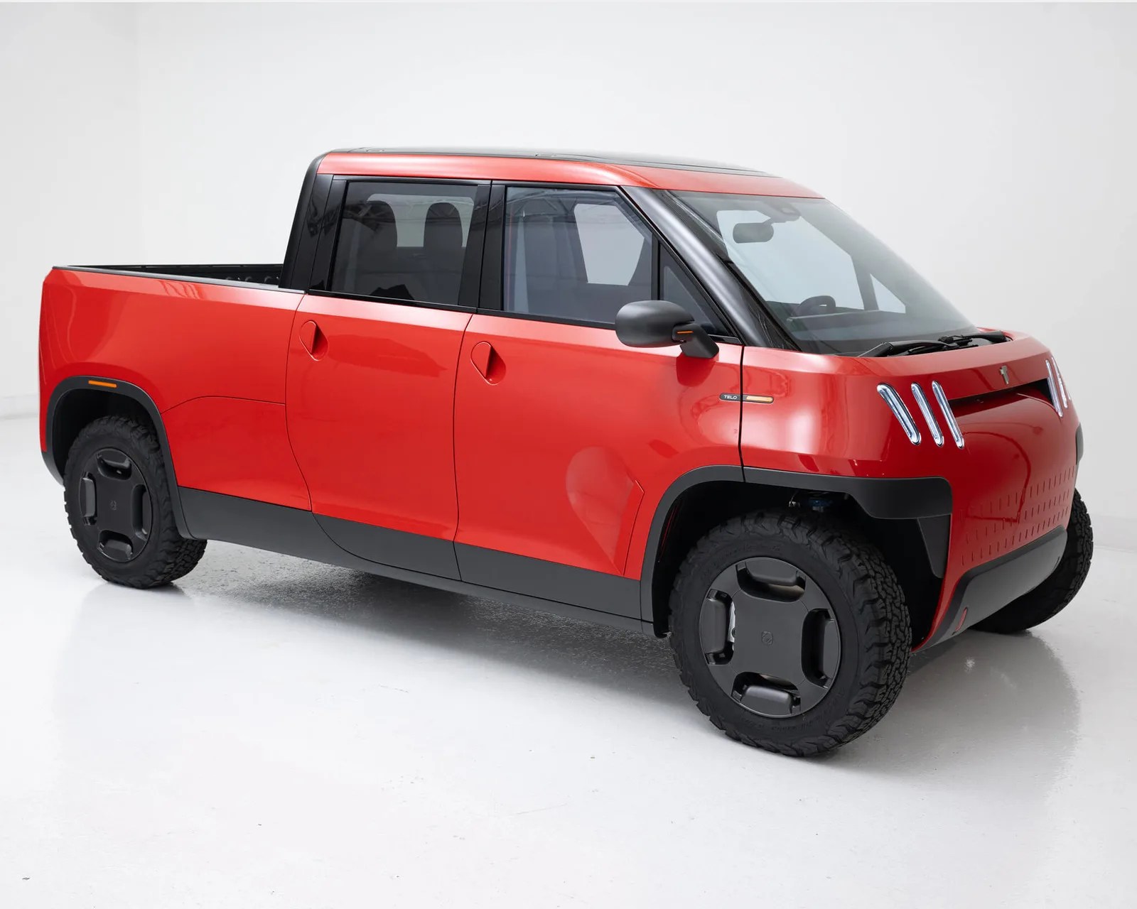 Red compact electric pickup truck with black trim and unique vertical LED headlights in a white studio.