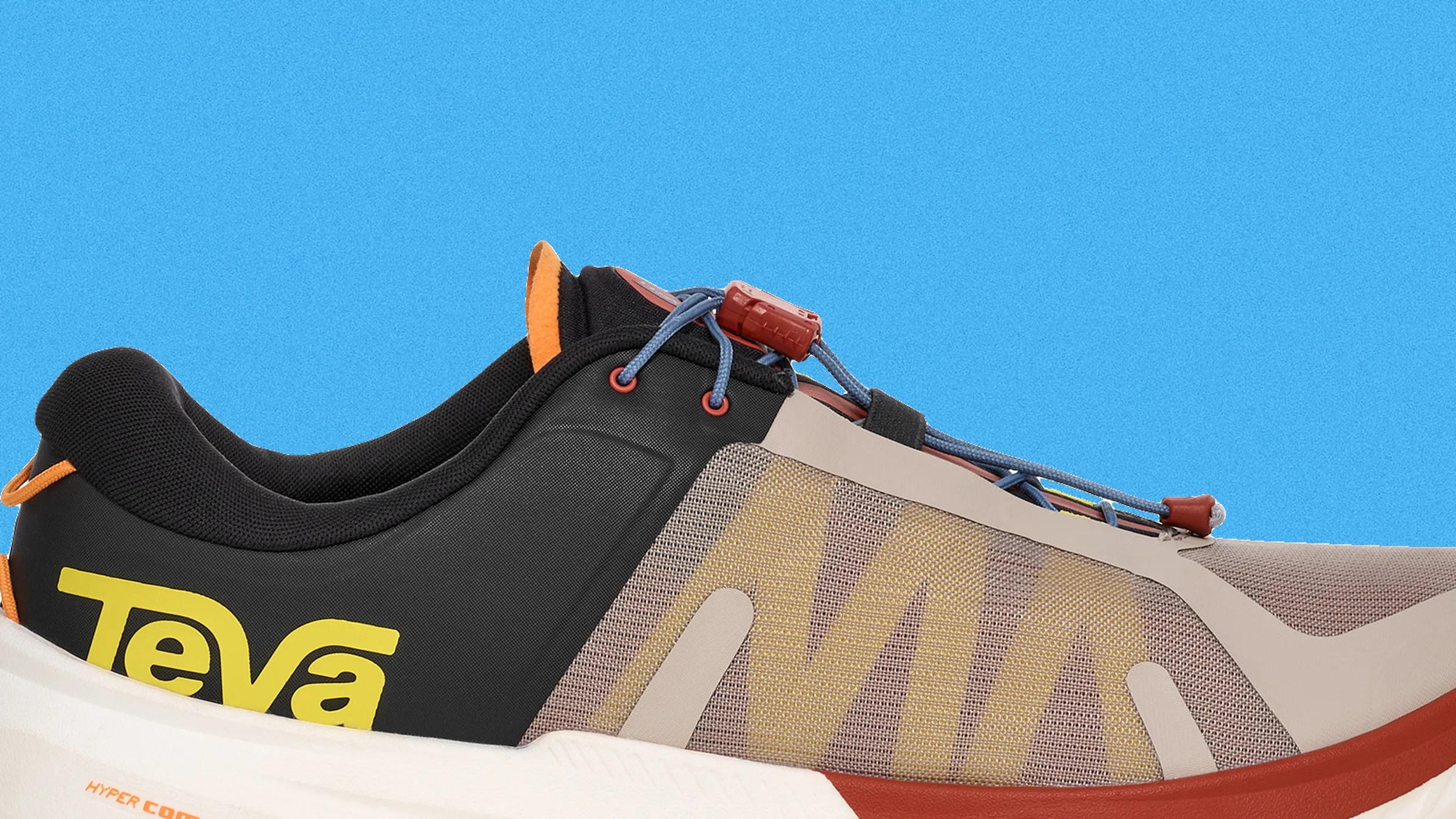 Close-up of a beige and black Teva sneaker with yellow logo, blue laces, and orange accents on a blue background.