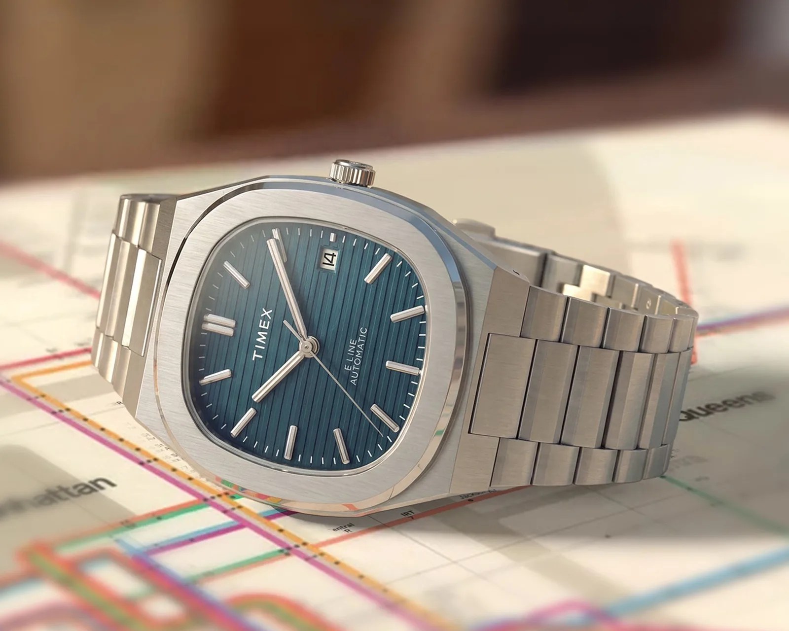 Silver stainless steel Timex wristwatch with a blue textured dial and date display on a map background.