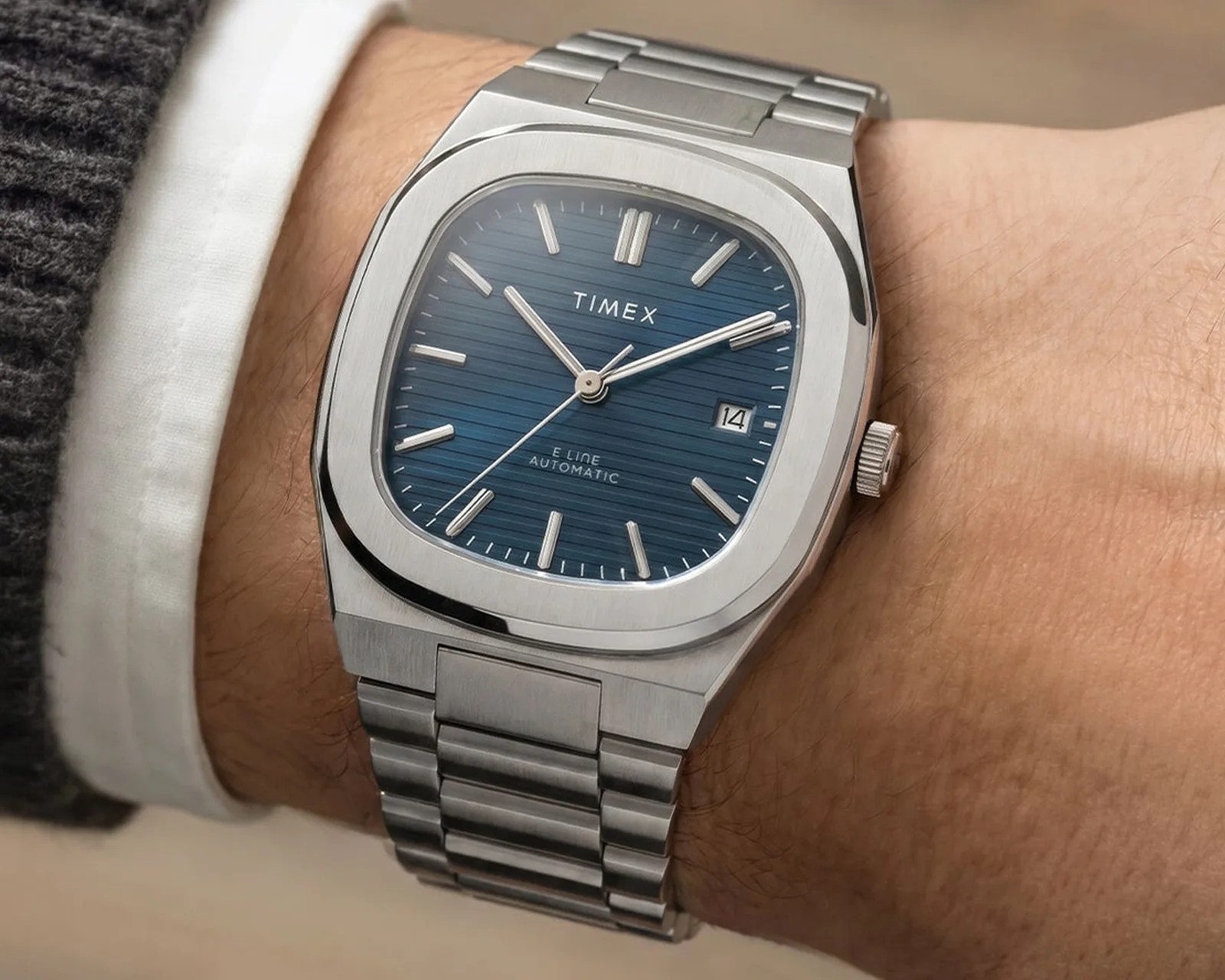 Silver stainless steel Timex wristwatch with a blue textured dial and date display worn on a wrist.