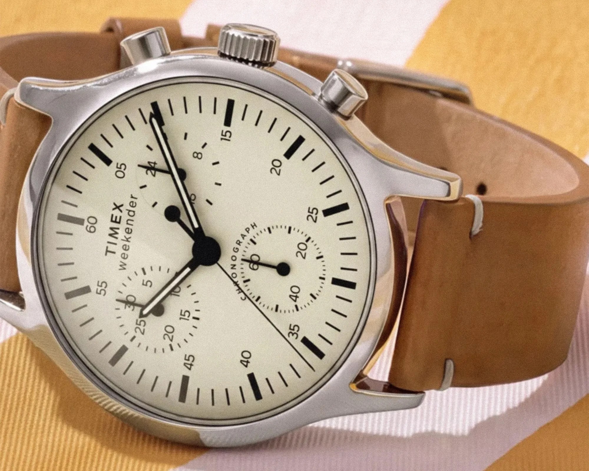 Timex Weekender chronograph watch with a silver case, cream dial, black markers, and tan leather strap.