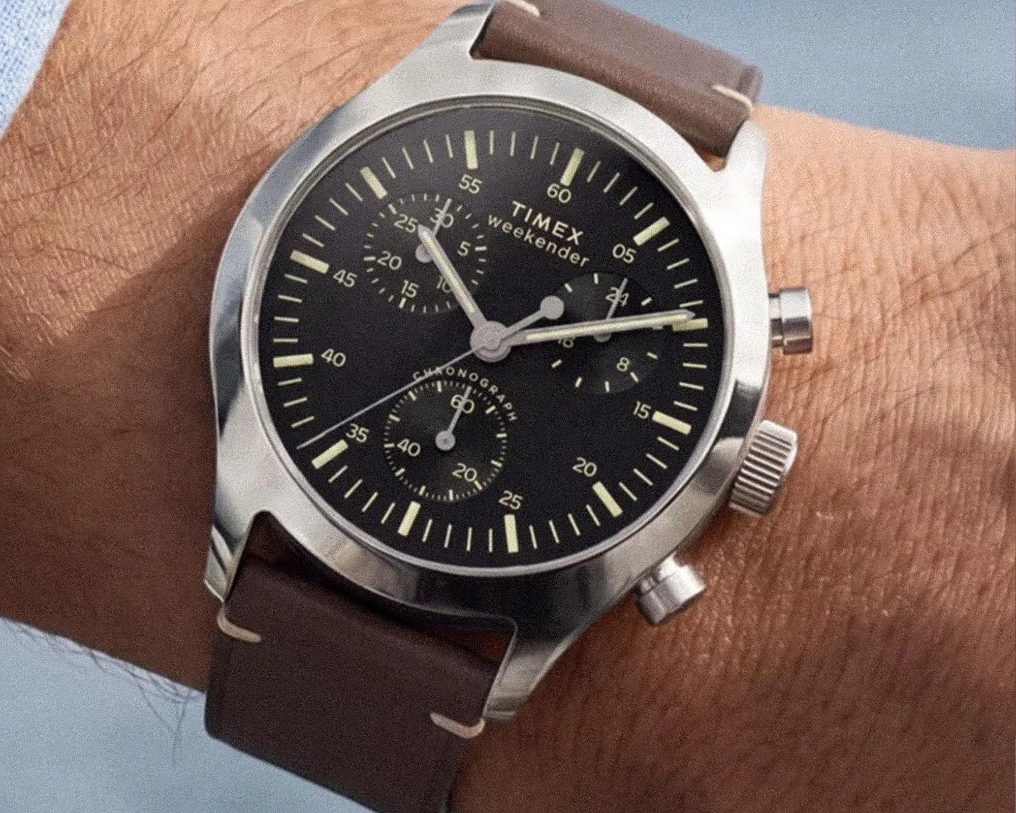 Timex Weekender chronograph watch with black dial, silver case, and brown leather strap on a wrist.