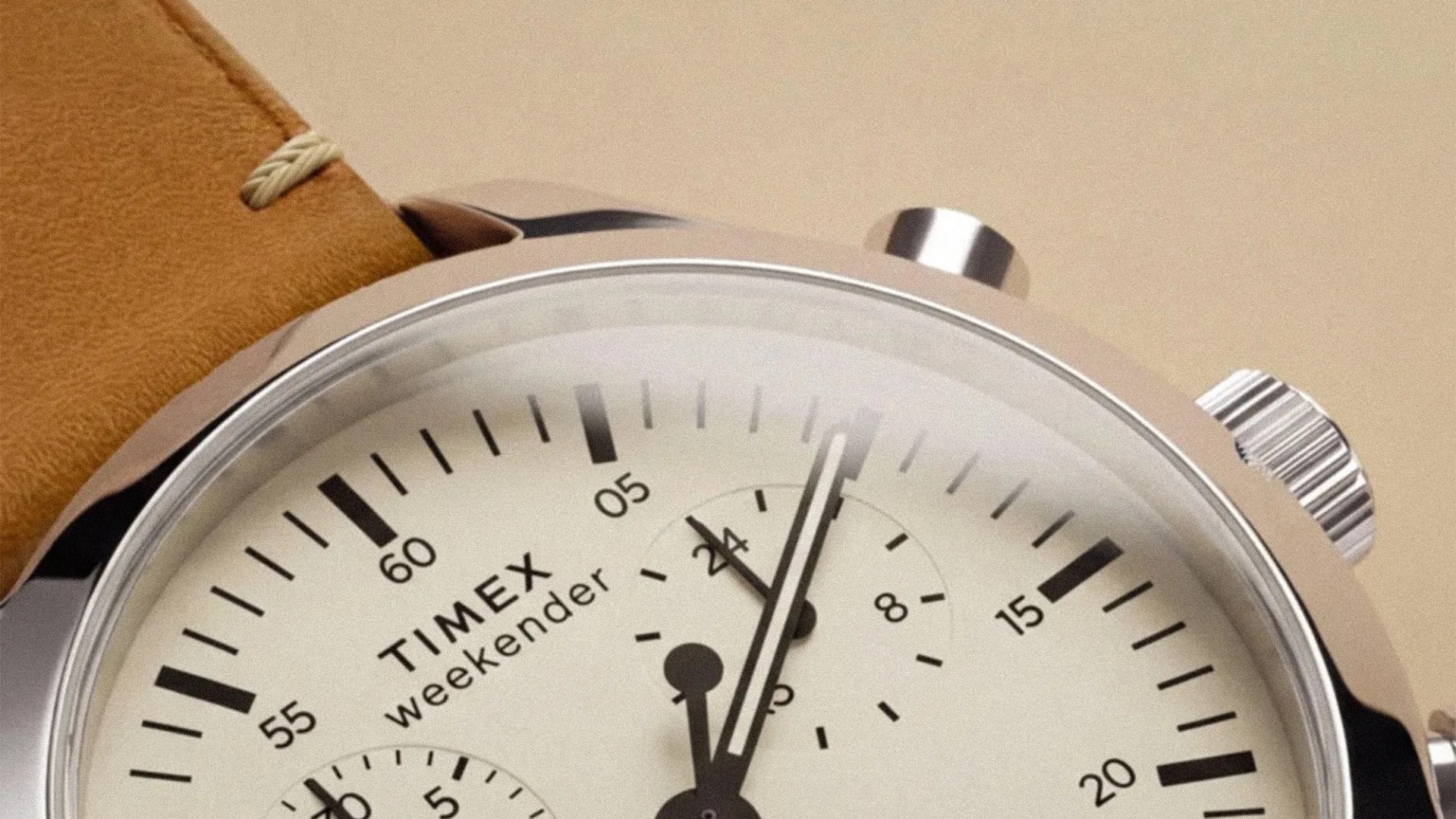 Close-up of a Timex Weekender watch with a cream dial, black markers, and a tan leather strap.