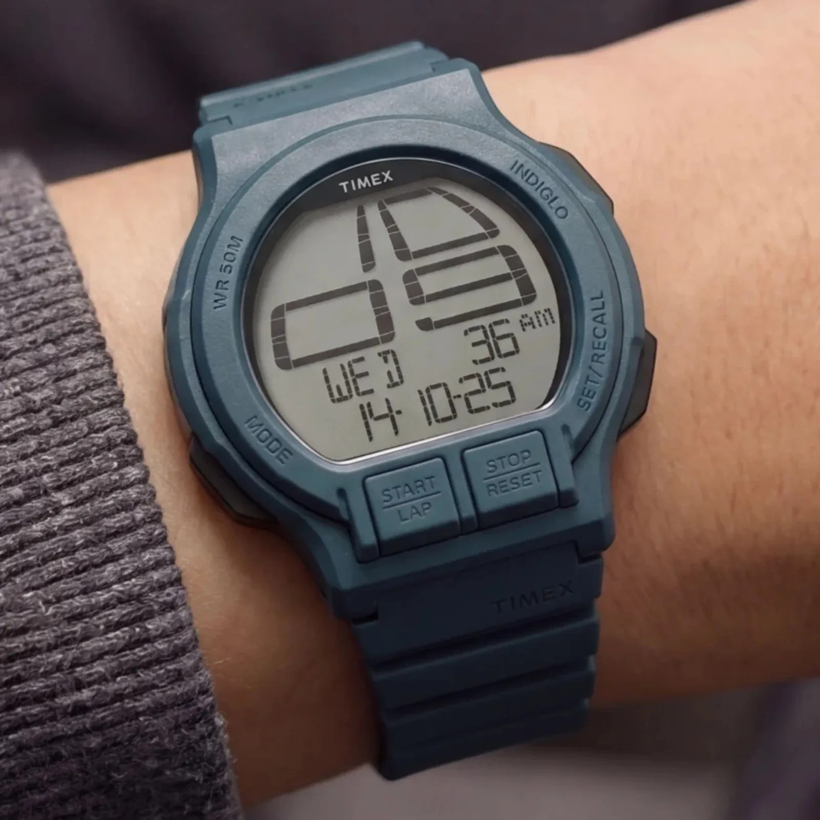 Blue Timex digital wristwatch with large display showing time, date, and buttons on a wrist.