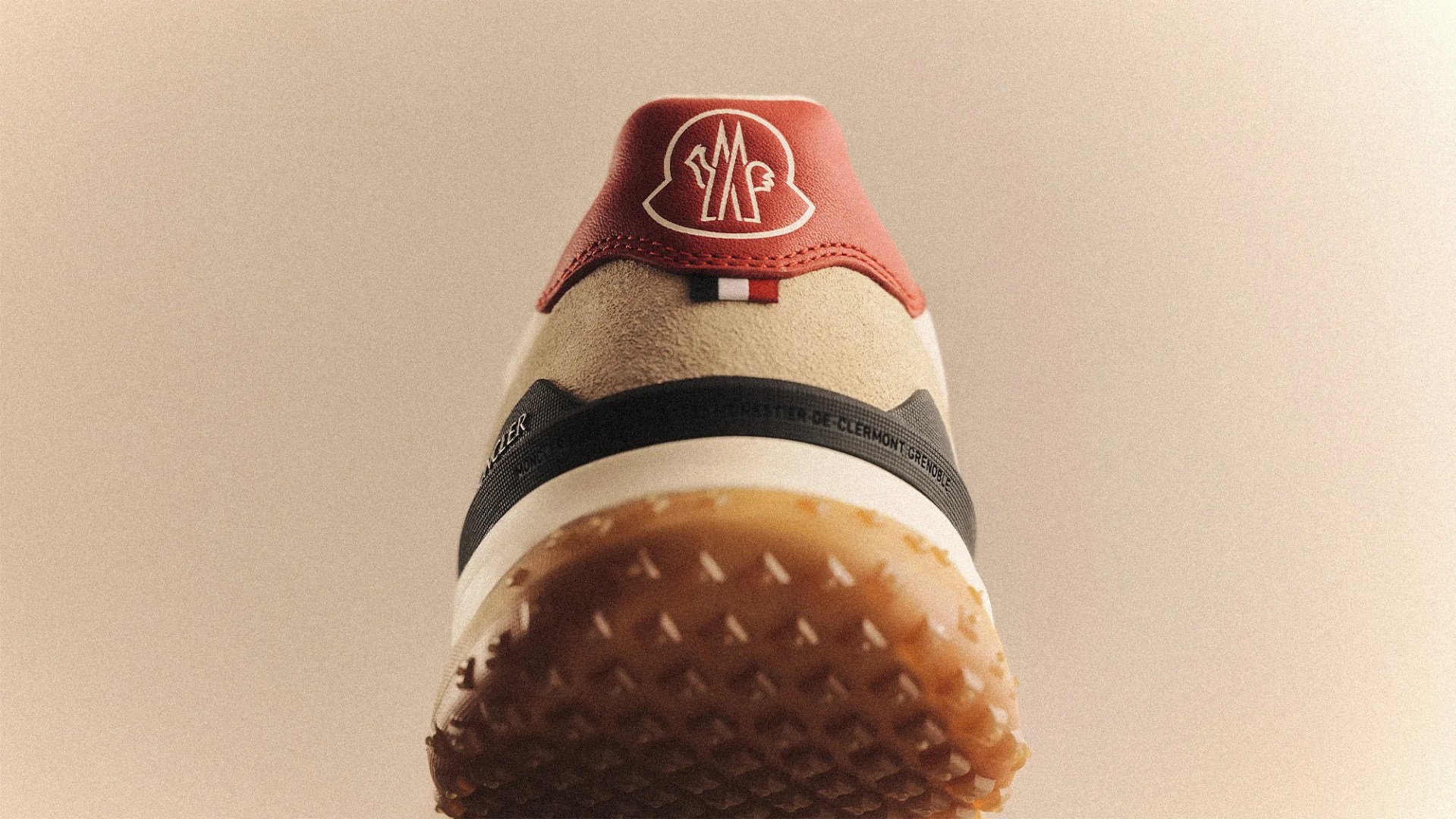 Close-up of the back heel of a beige and red sneaker with a textured gum sole and a logo on the red heel tab.