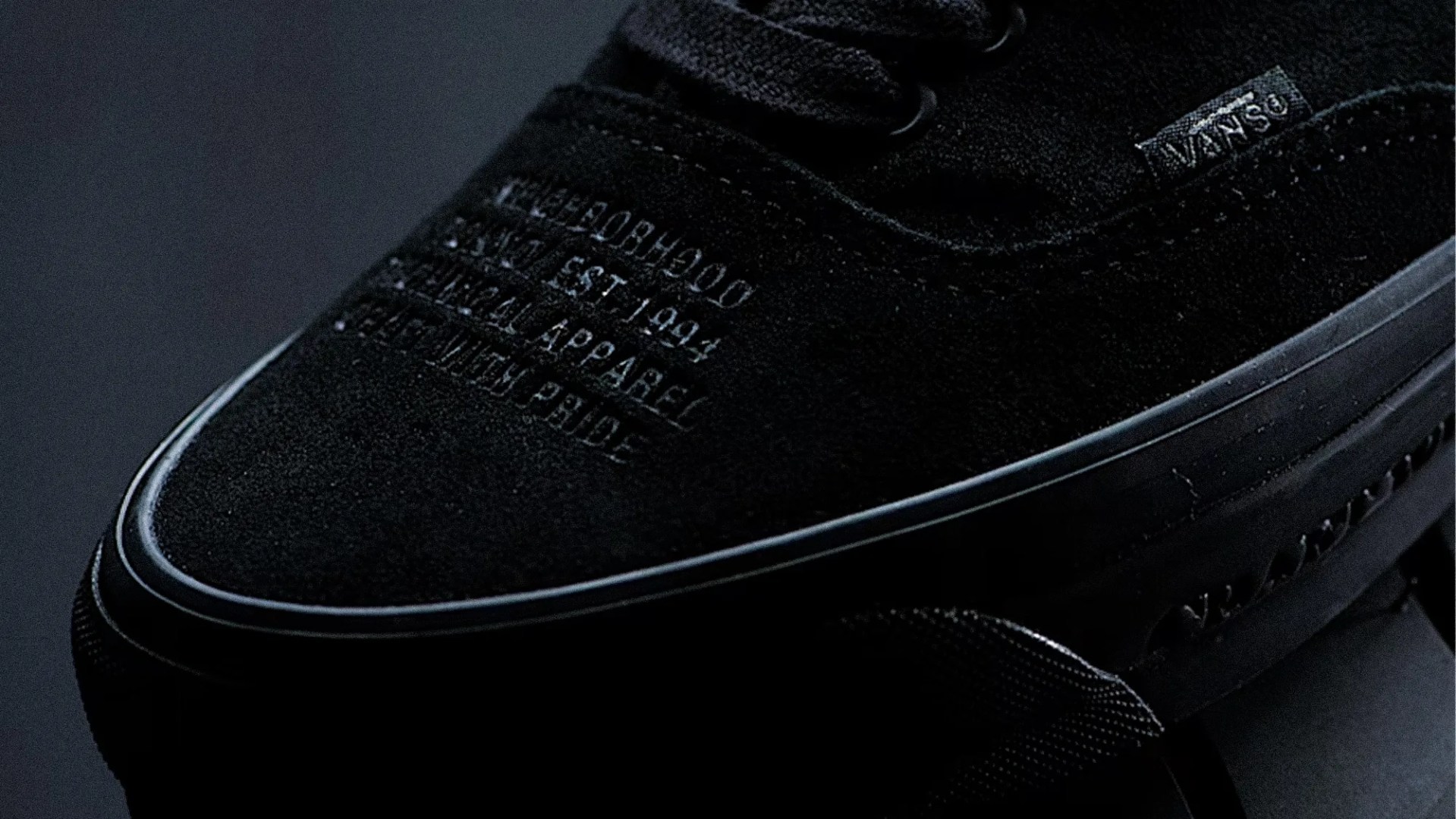 Close-up of black Vans suede sneaker with embossed text and Vans logo tag on the side.