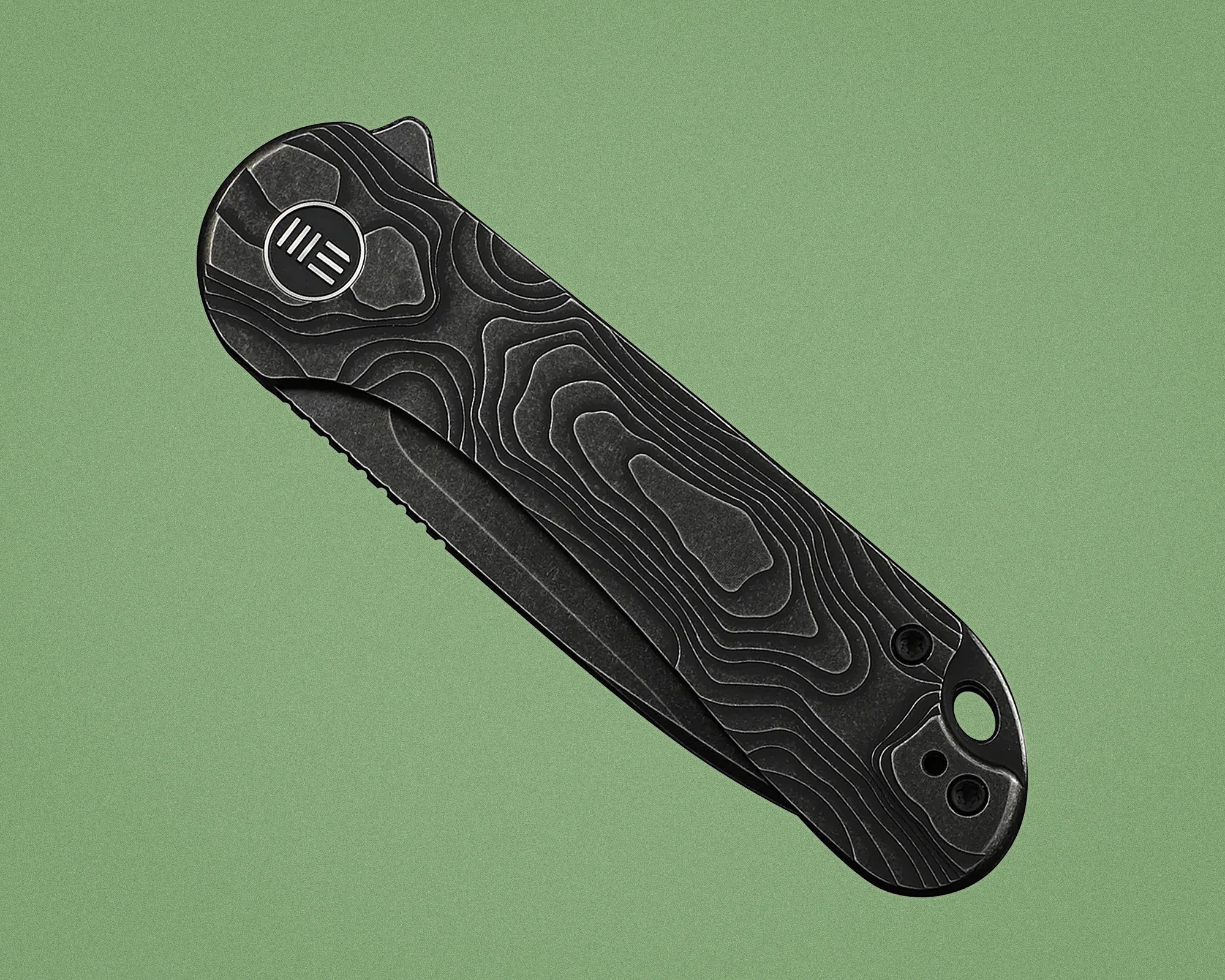 Black folding knife handle with topographic contour pattern and circular logo on a green background.