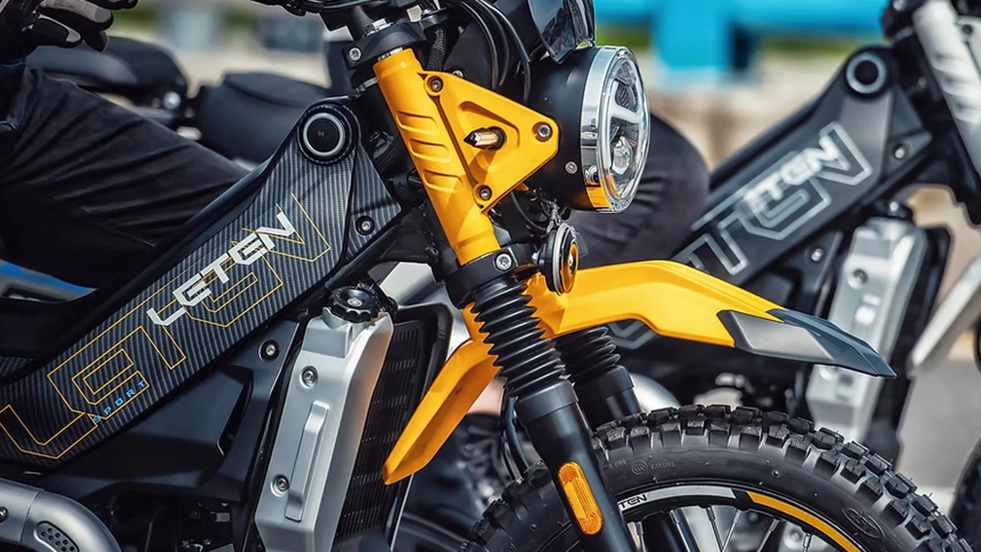 Close-up of a black and yellow electric motorcycle front suspension and headlight with "LGETEN" branding on the frame.