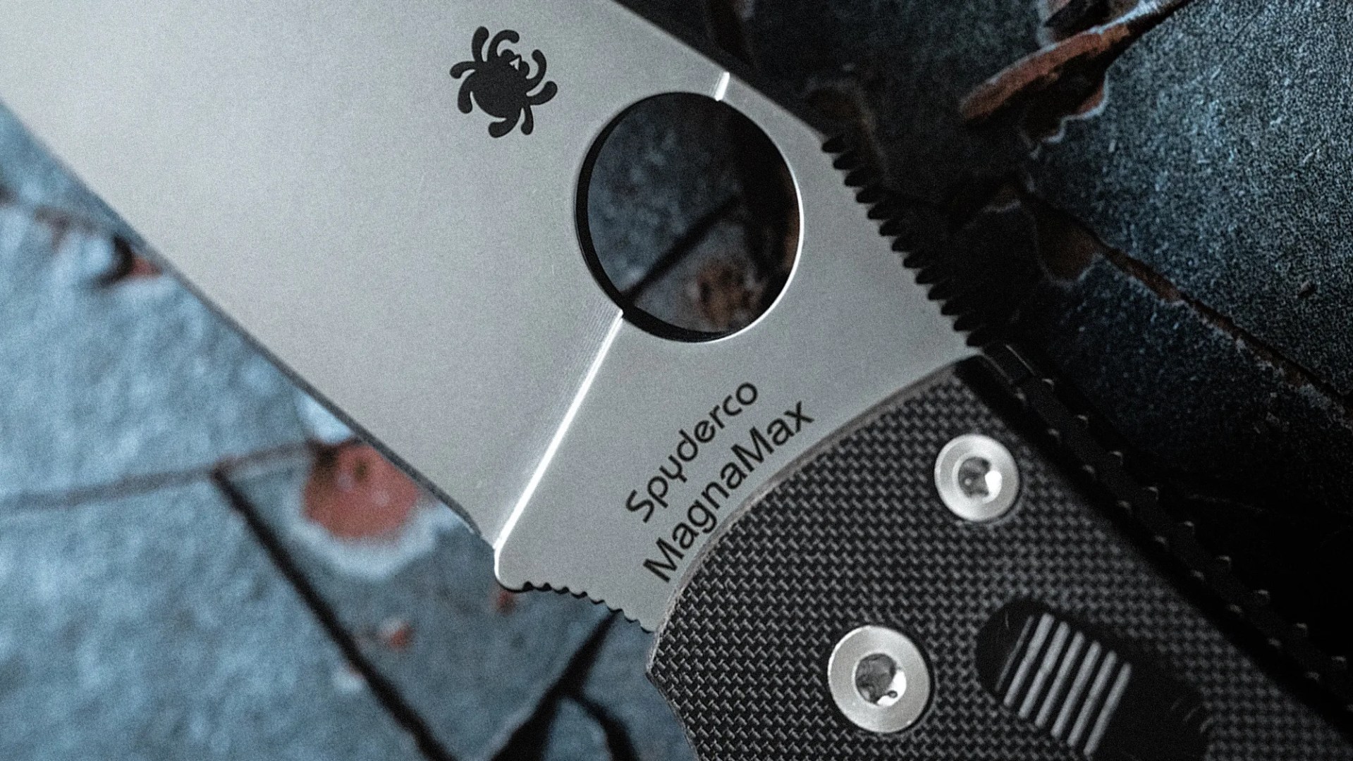 Close-up of a Spyderco MagnaMax folding knife blade with a circular hole and textured black handle.