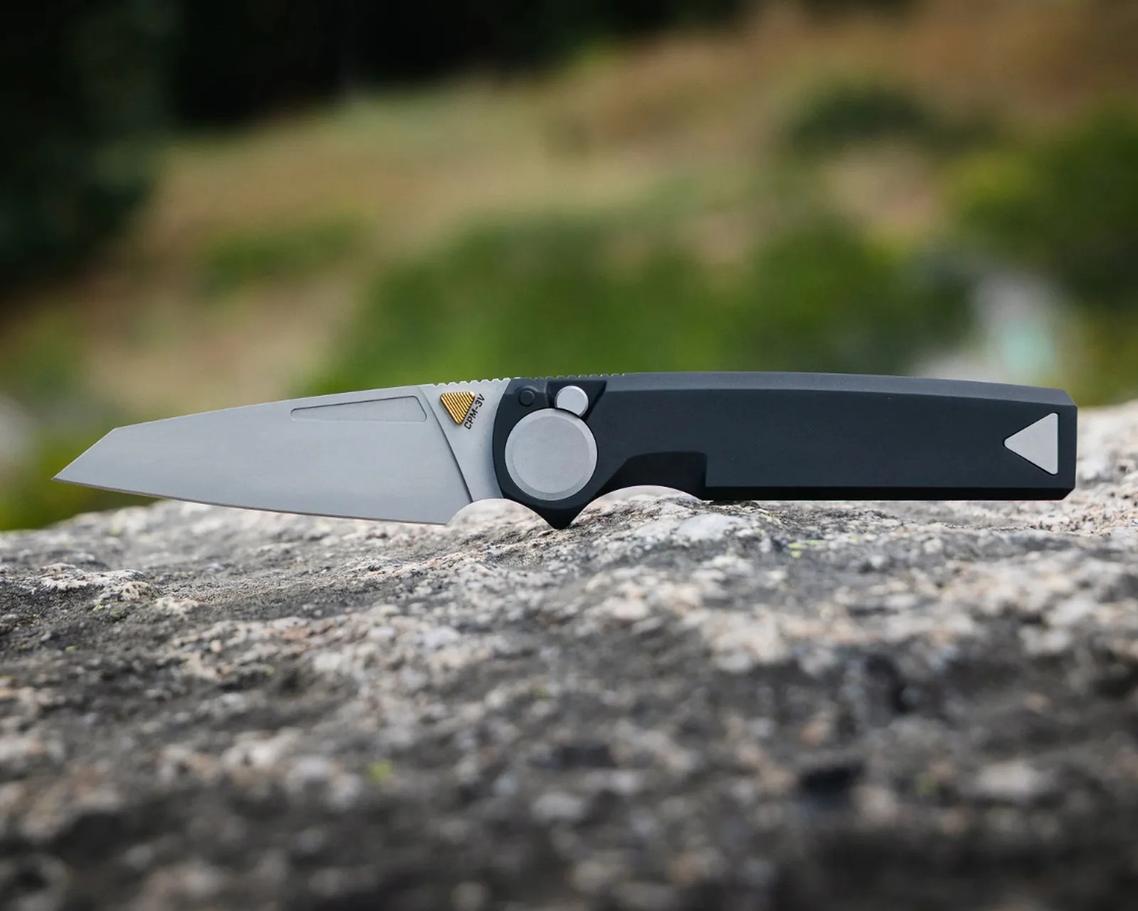 Folding knife with a matte silver blade and black handle resting on a rock.